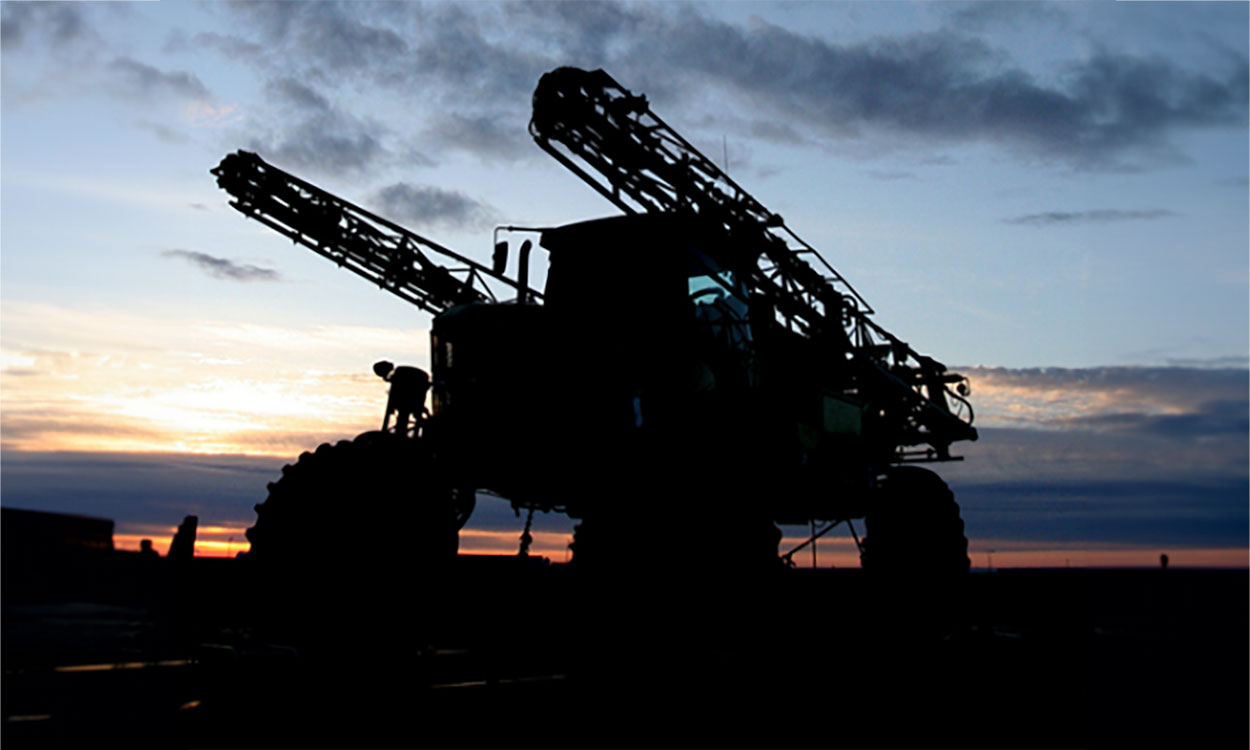 Ground sprayer parked outside a field at sunset.
