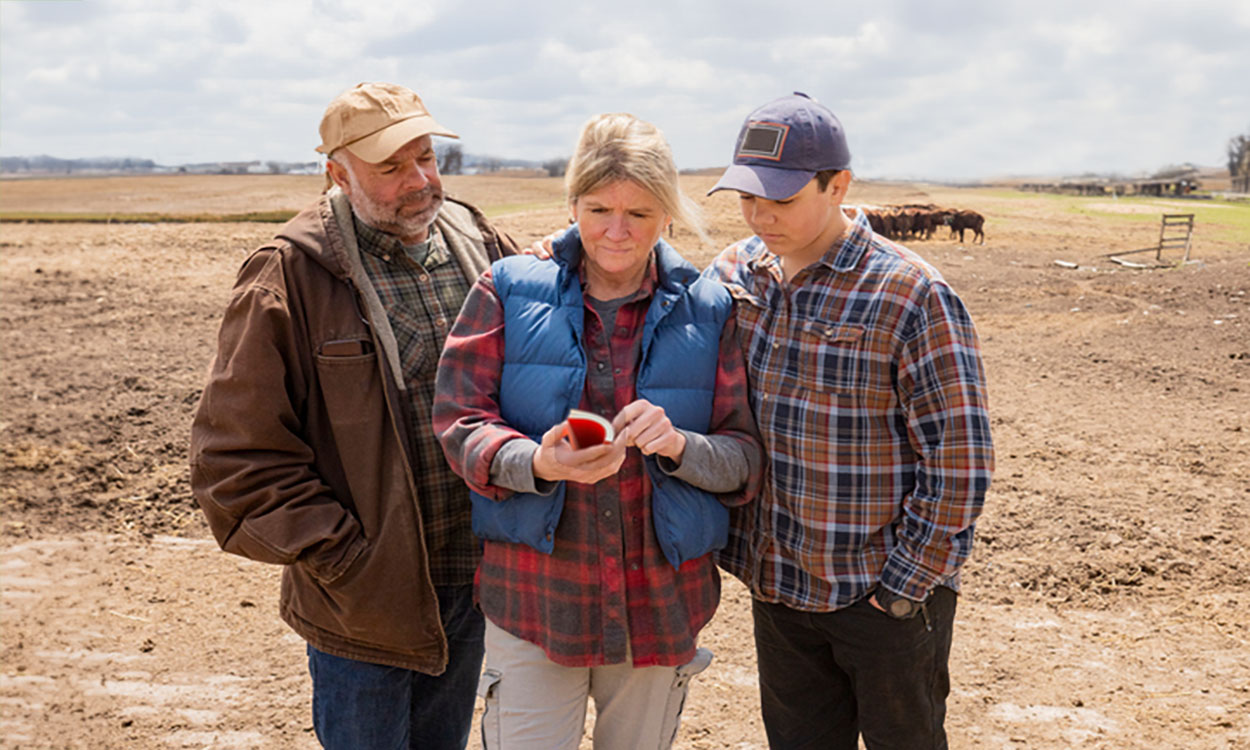 Ranch family examining a red calving record book near a herd of cattle.