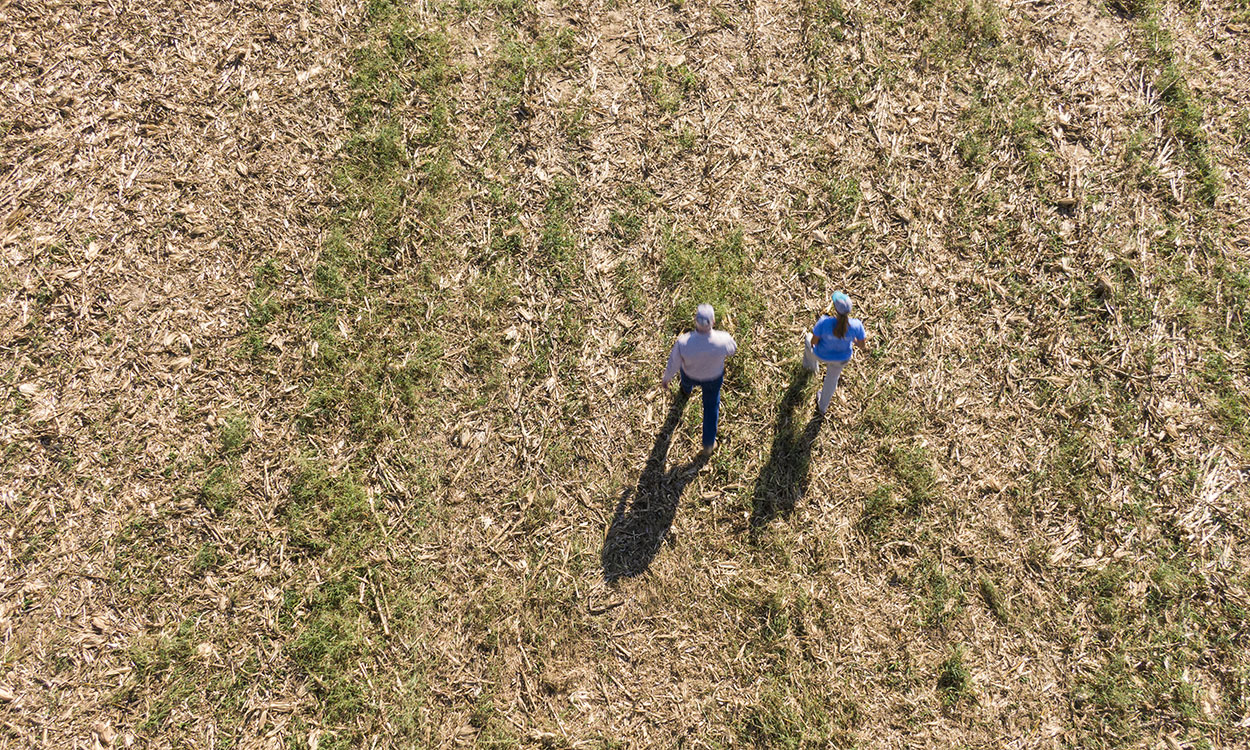 Aerial view of two producers walking through a field with abundant crop residue.