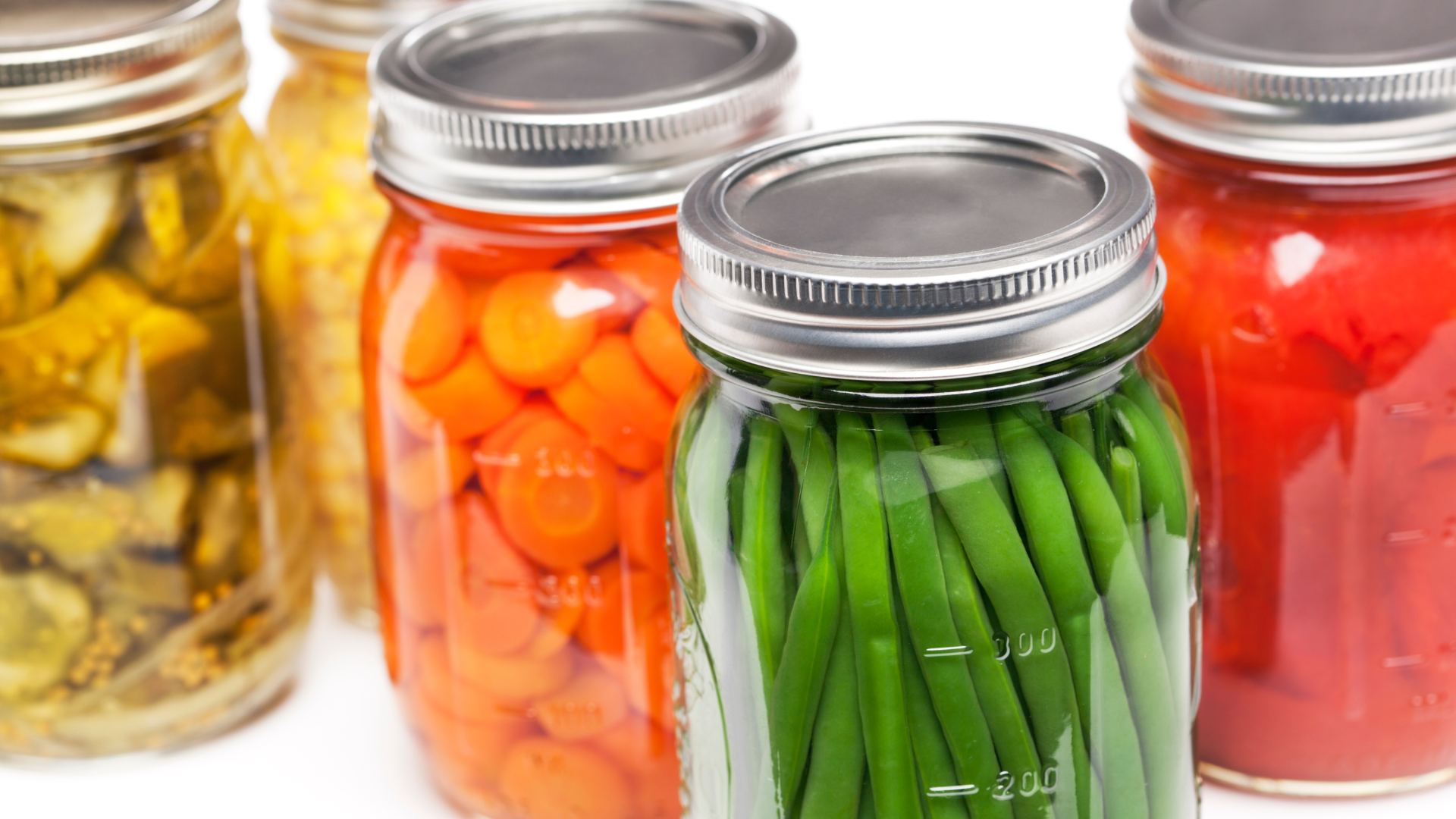 Jars of canned green beans, carrots, tomatoes, cucumbers and corn