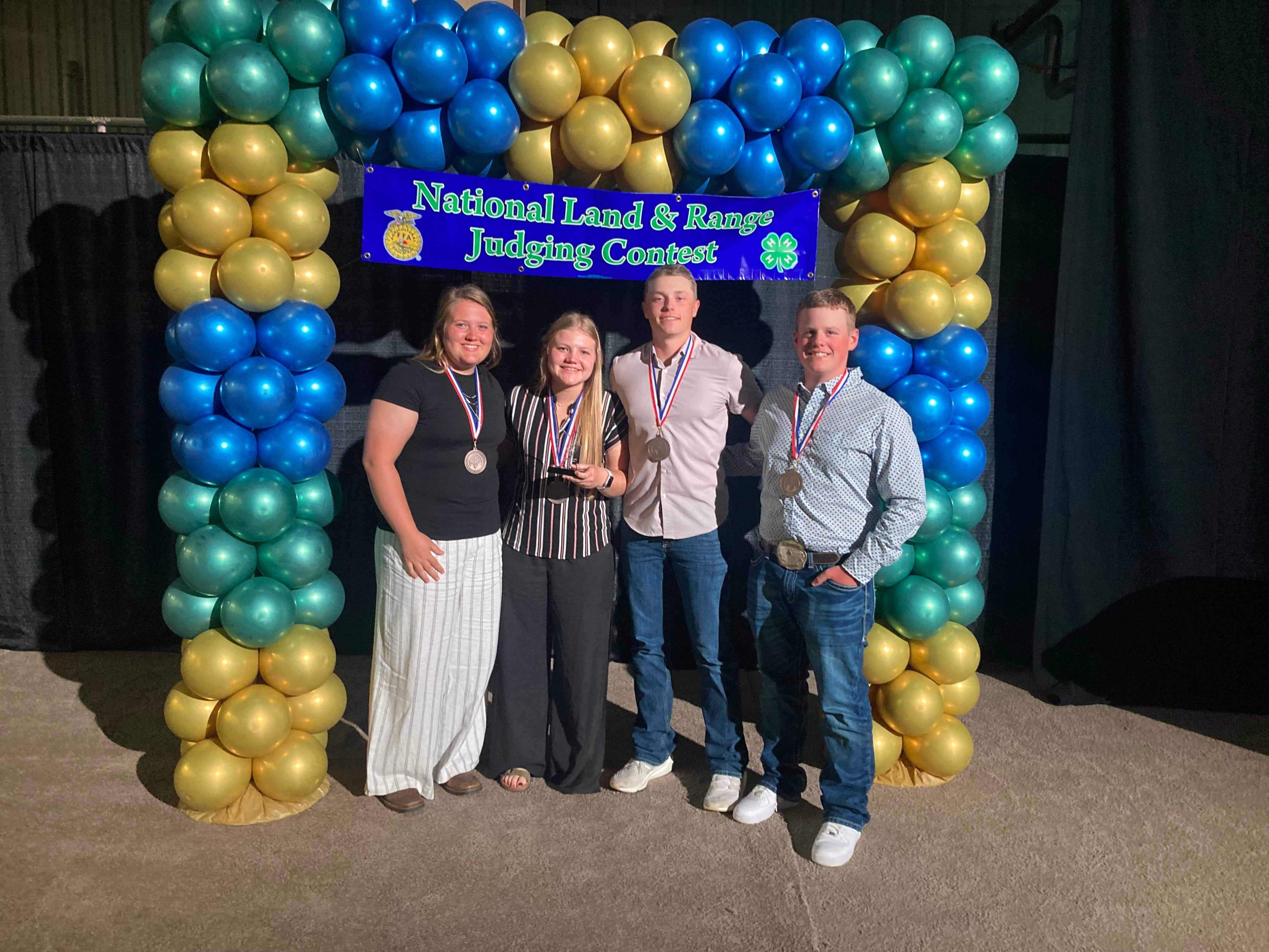 Four people stand in front of a balloon archway and a banner that says "National Land and Range Judging Contest"