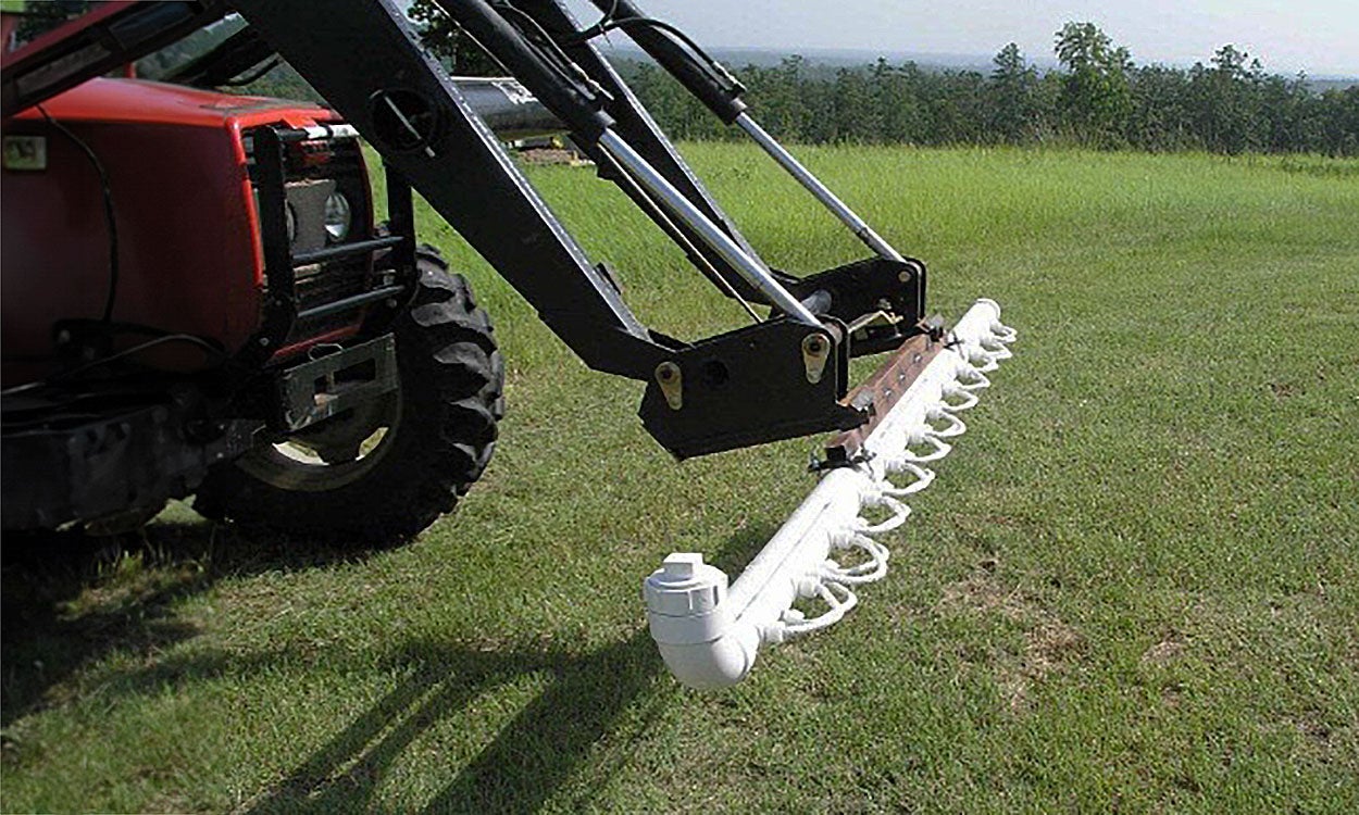White PVC pipe with a white cotton rope attached and a larger, white PVC apparatus with multiple, white, cotton ropes attached, suspended above green grass.