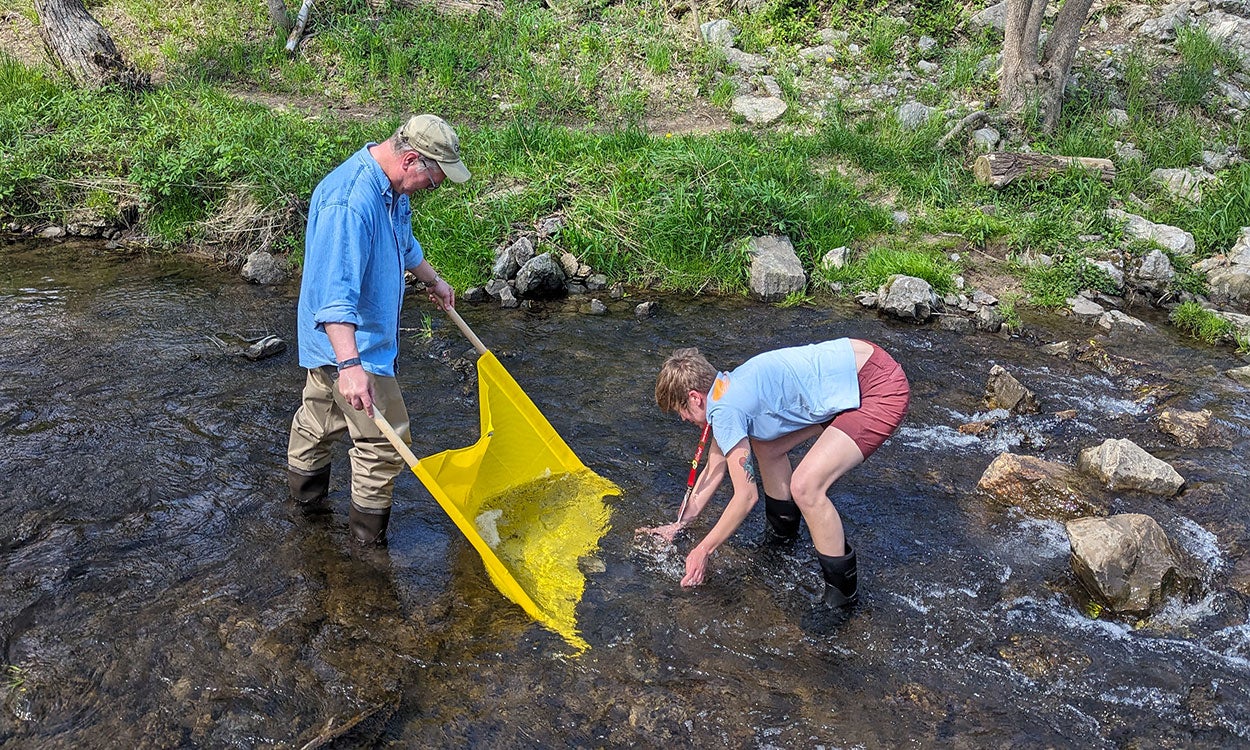 A man and woman using a kick seine to sample aquatic invertebrates from a stream.