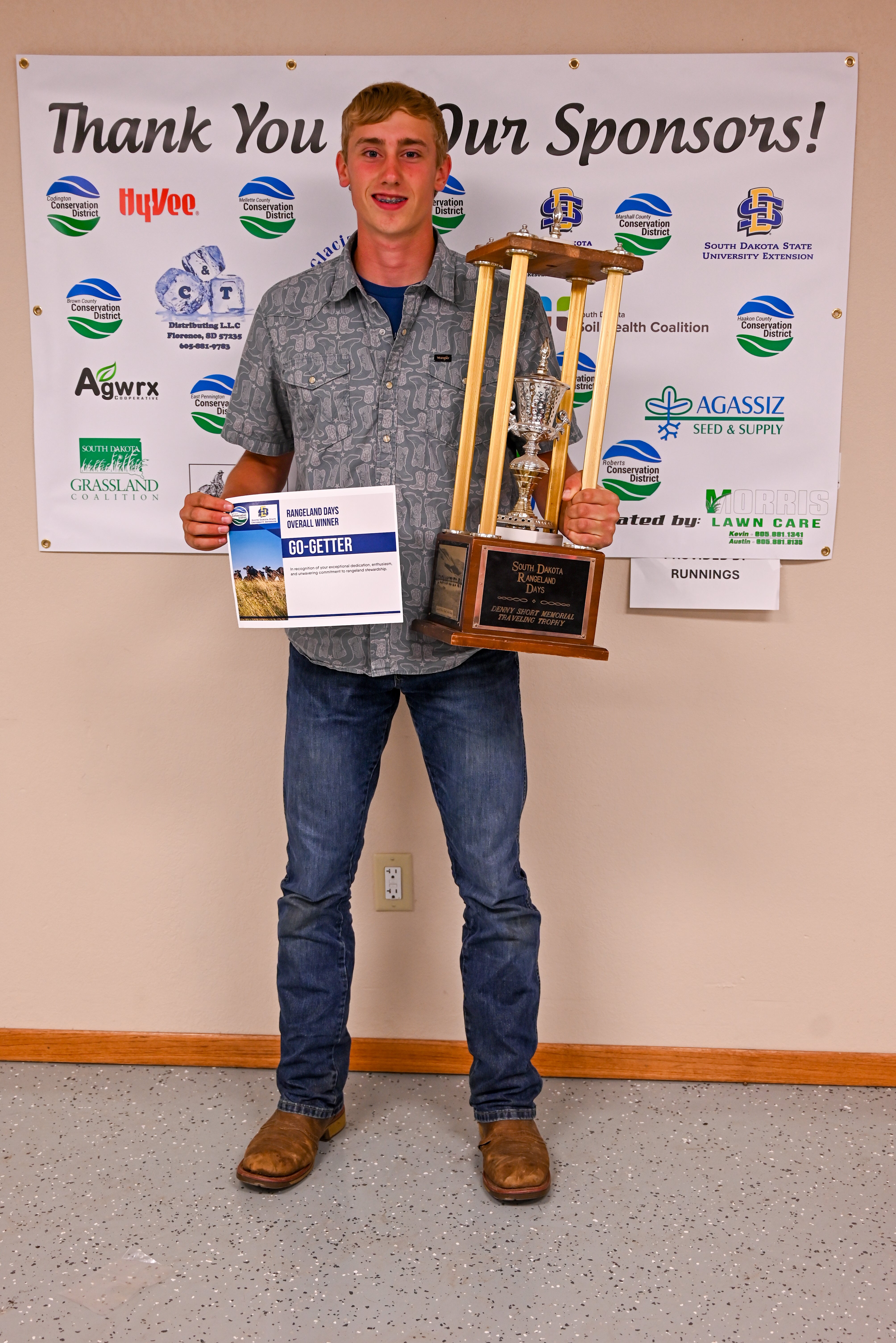 Adrik Schoon A youth stands with a large trophy and certificate that says "Go-Getter"