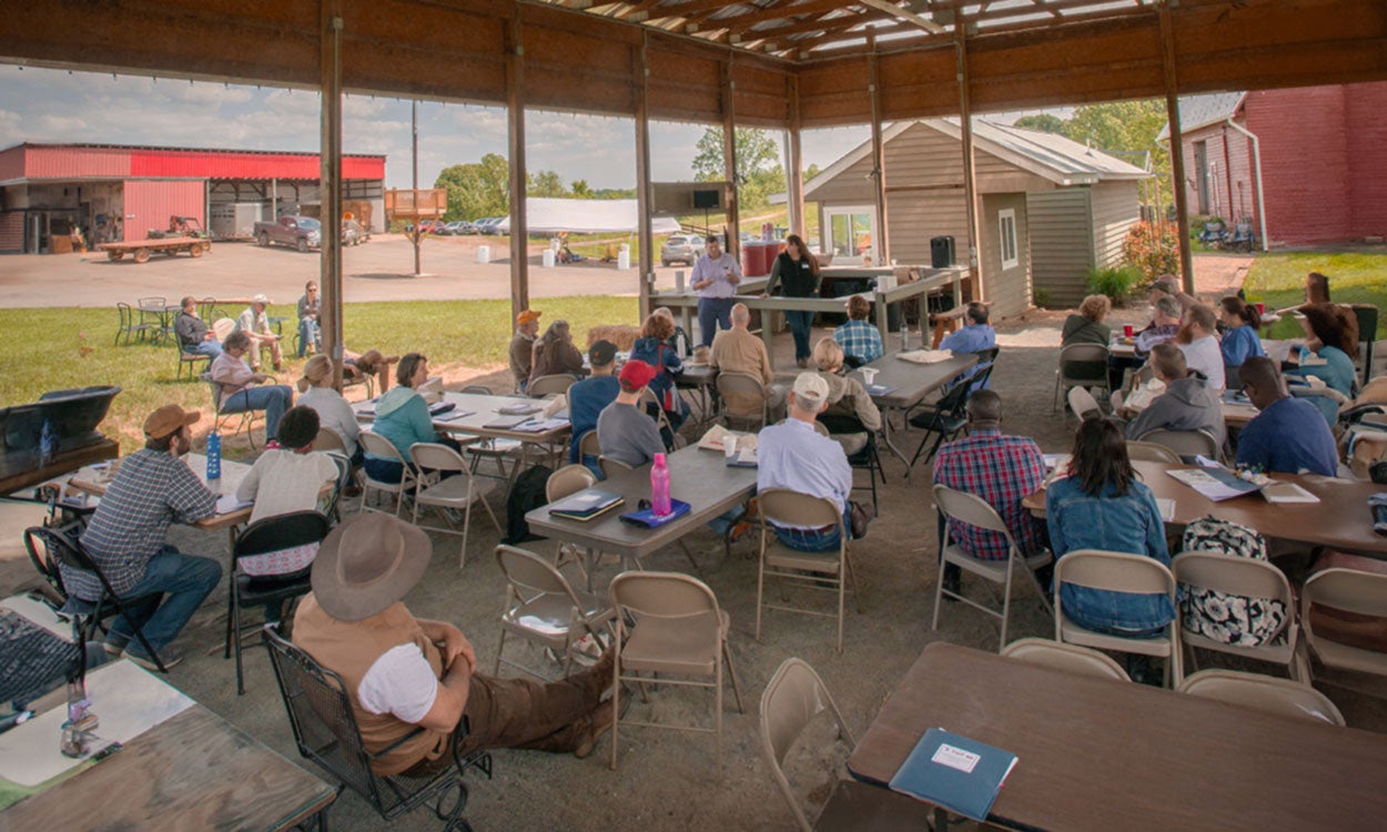 Community members meeting in an outdoor picnic shelter near a farm.