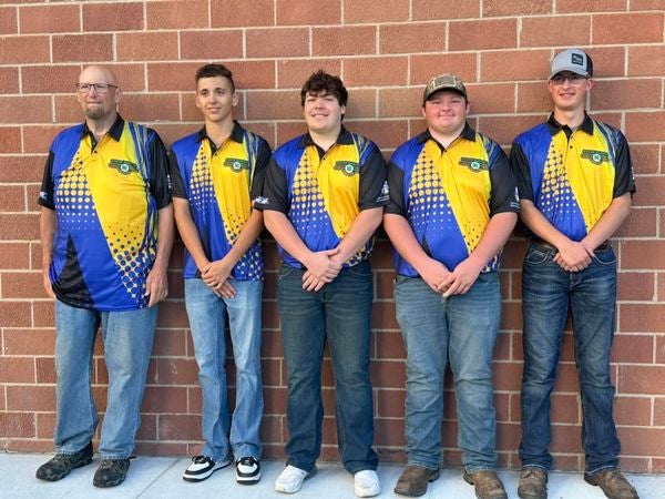 Four youth and their coach stand in front of a brick wall and smile for the camera