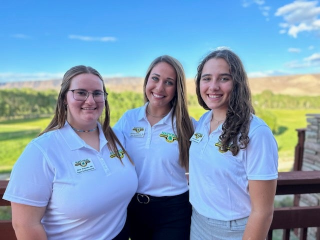 Three girls wearing shirts with National Shooting Sports insignia smile for the camera