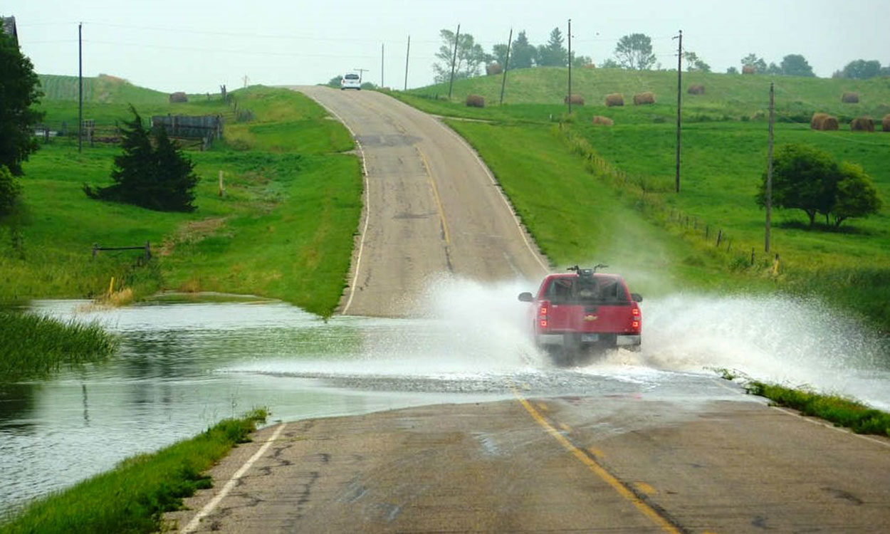 Flood waters obstructing a paved country road.