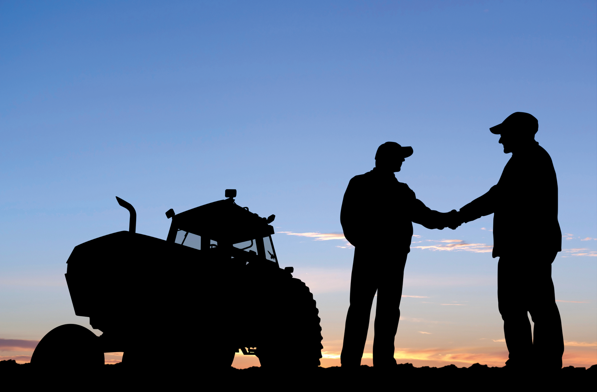 Sihlouette of farmers shaking hands with a tractor in the background