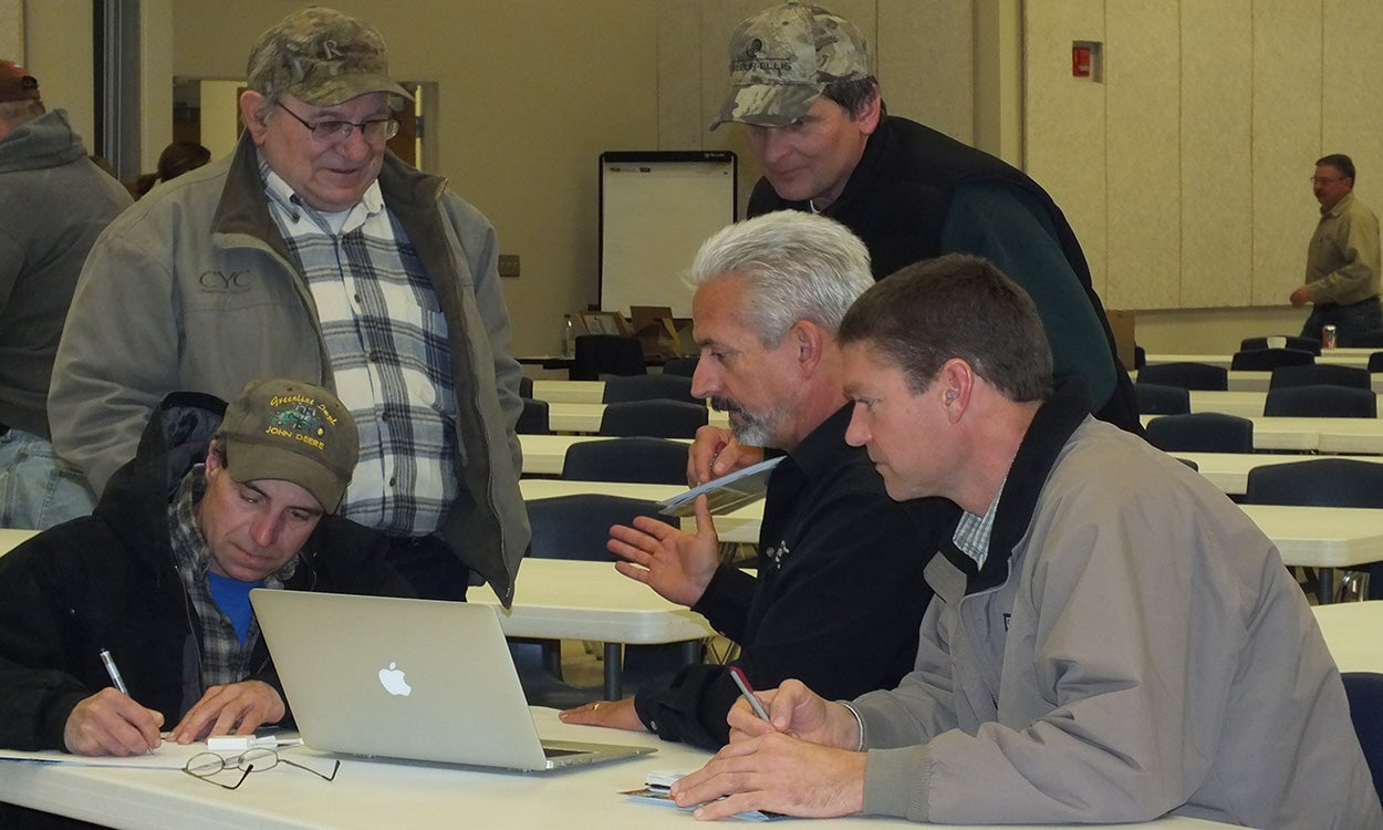 Group of producers gathered around a laptop at a training event.