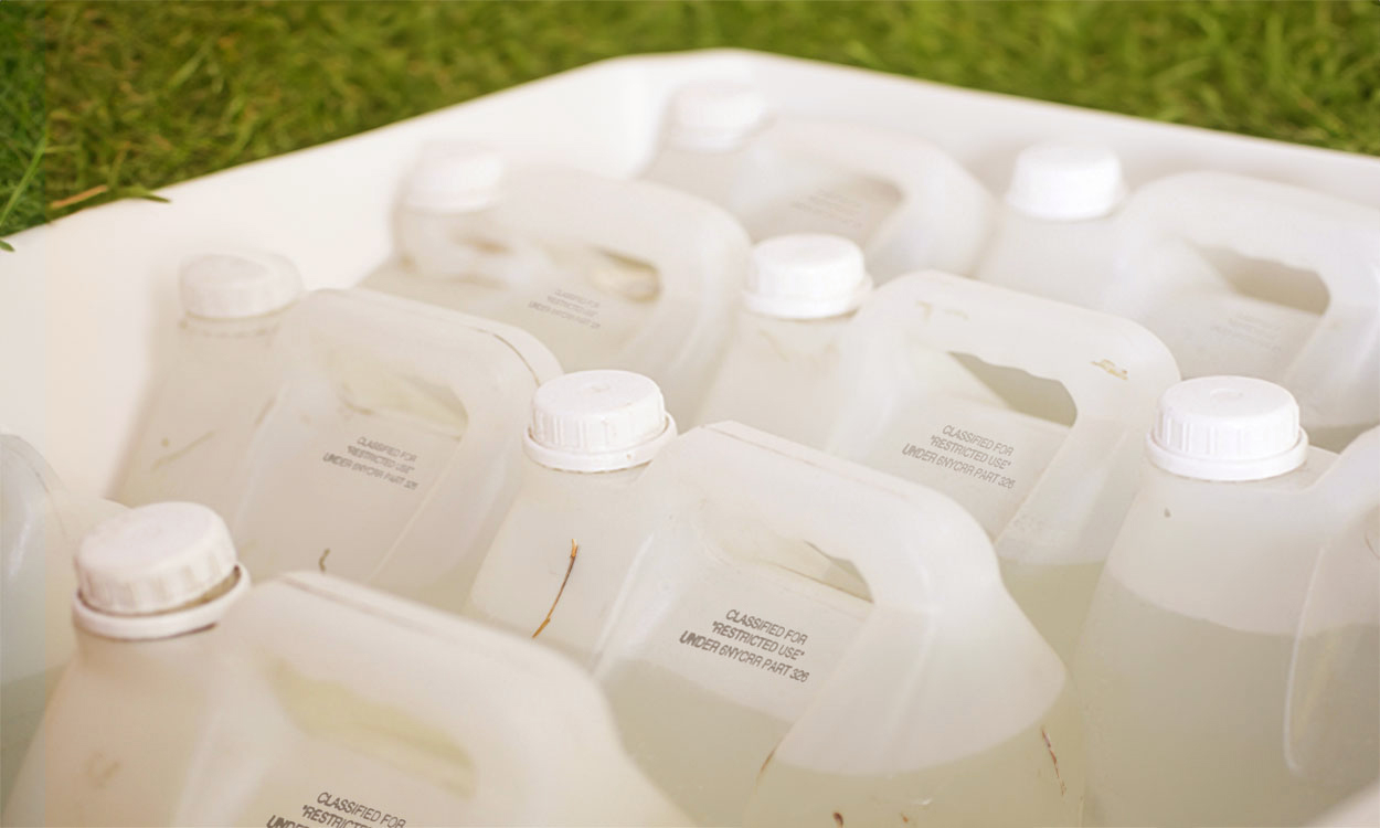 Several plastic bottles of pesticides gathered together in a white tub.
