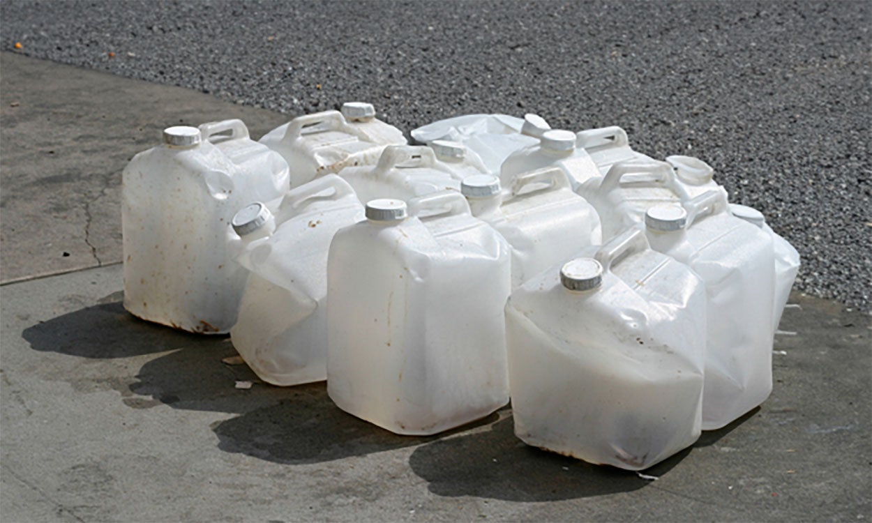 Several damaged plastic pesticide containers grouped together on a driveway.