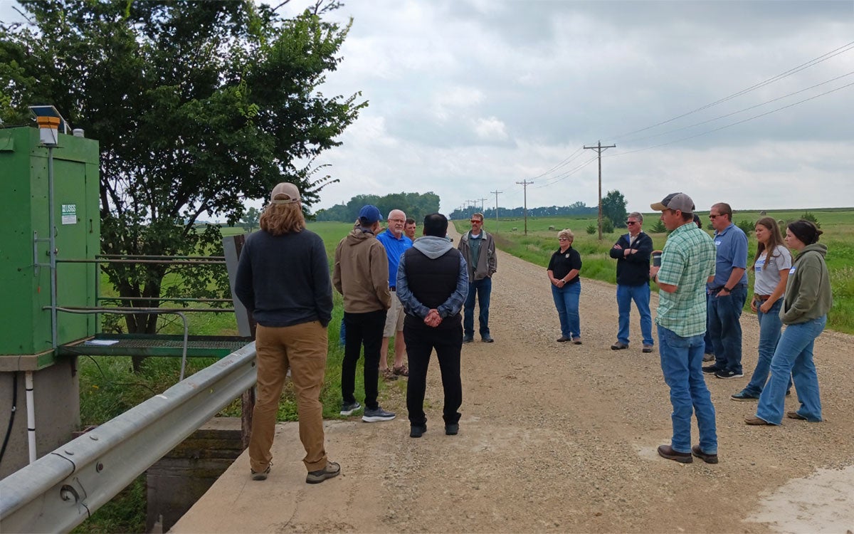 Watershed Academy attendees discussing riparian area management in the countryside on a bridge over a waterway.