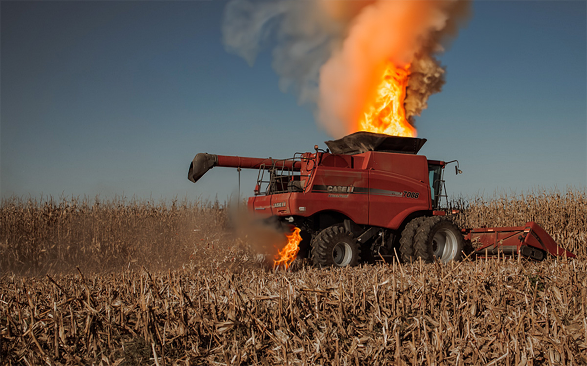 Red combine catching on fire while harvesting corn.