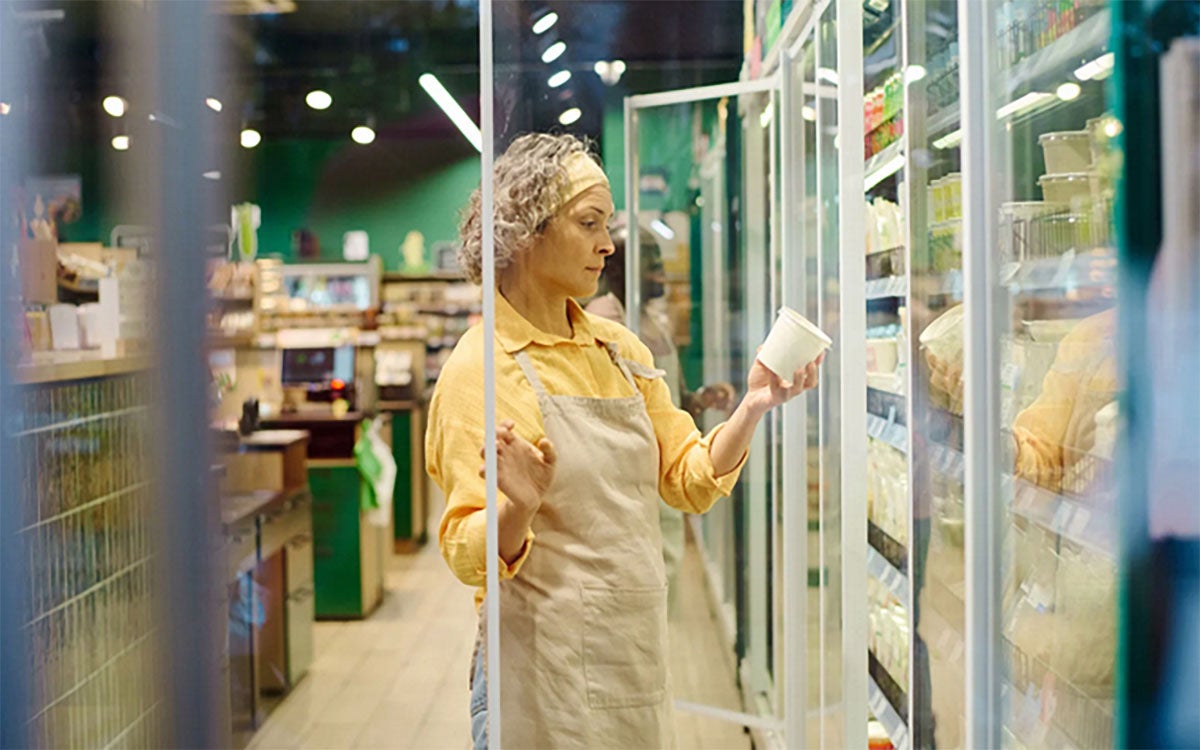 Grocery store employee reviewing the label on a carton of yogurt.