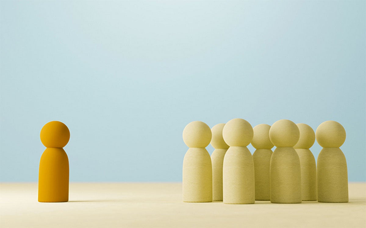 A single, gold wooden figure stands before a group of several wood figures, symbolizing the autocratic leadership style.