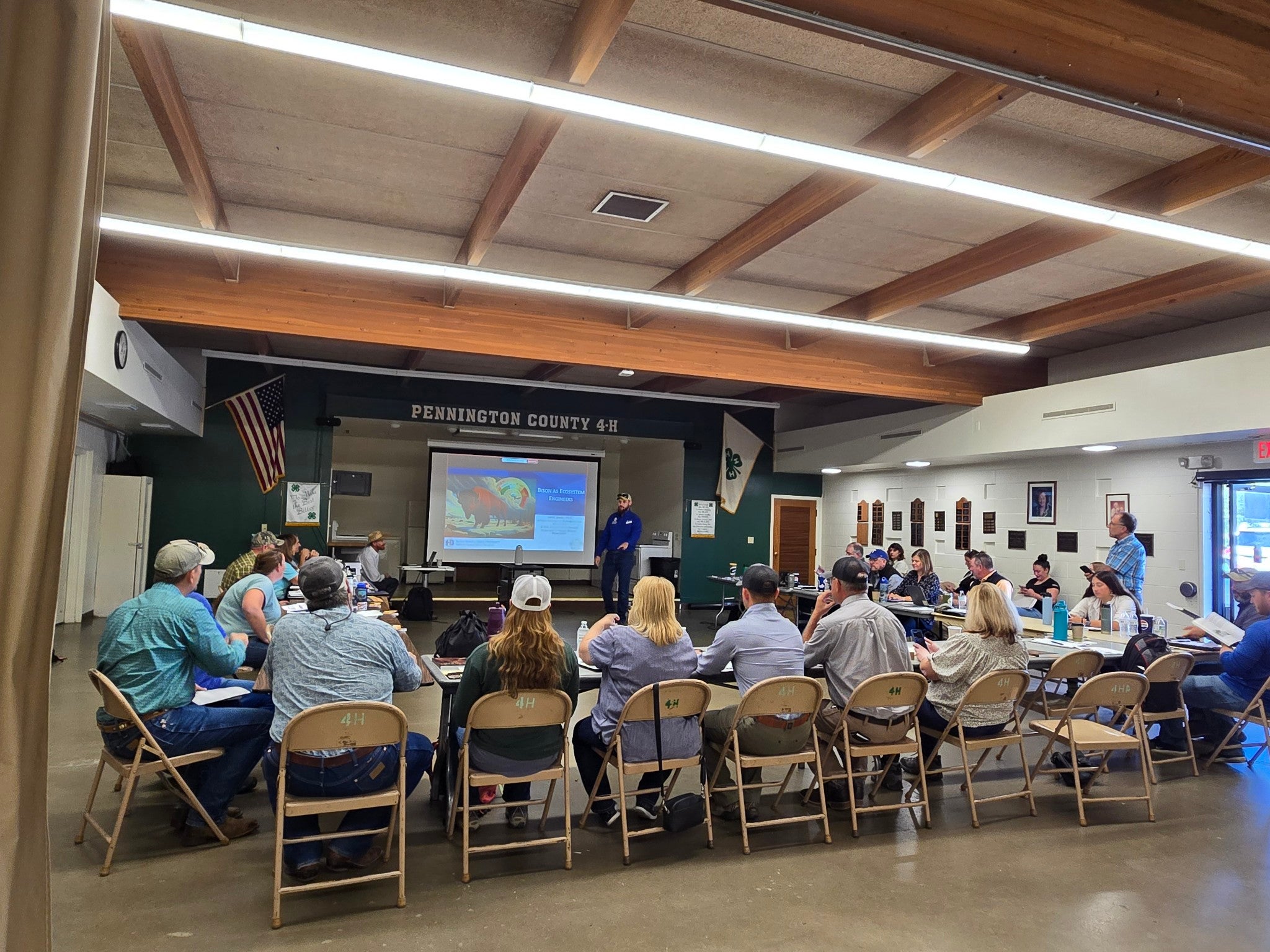 A man stands in front of a PowerPoint, giving a presentation to a room of people