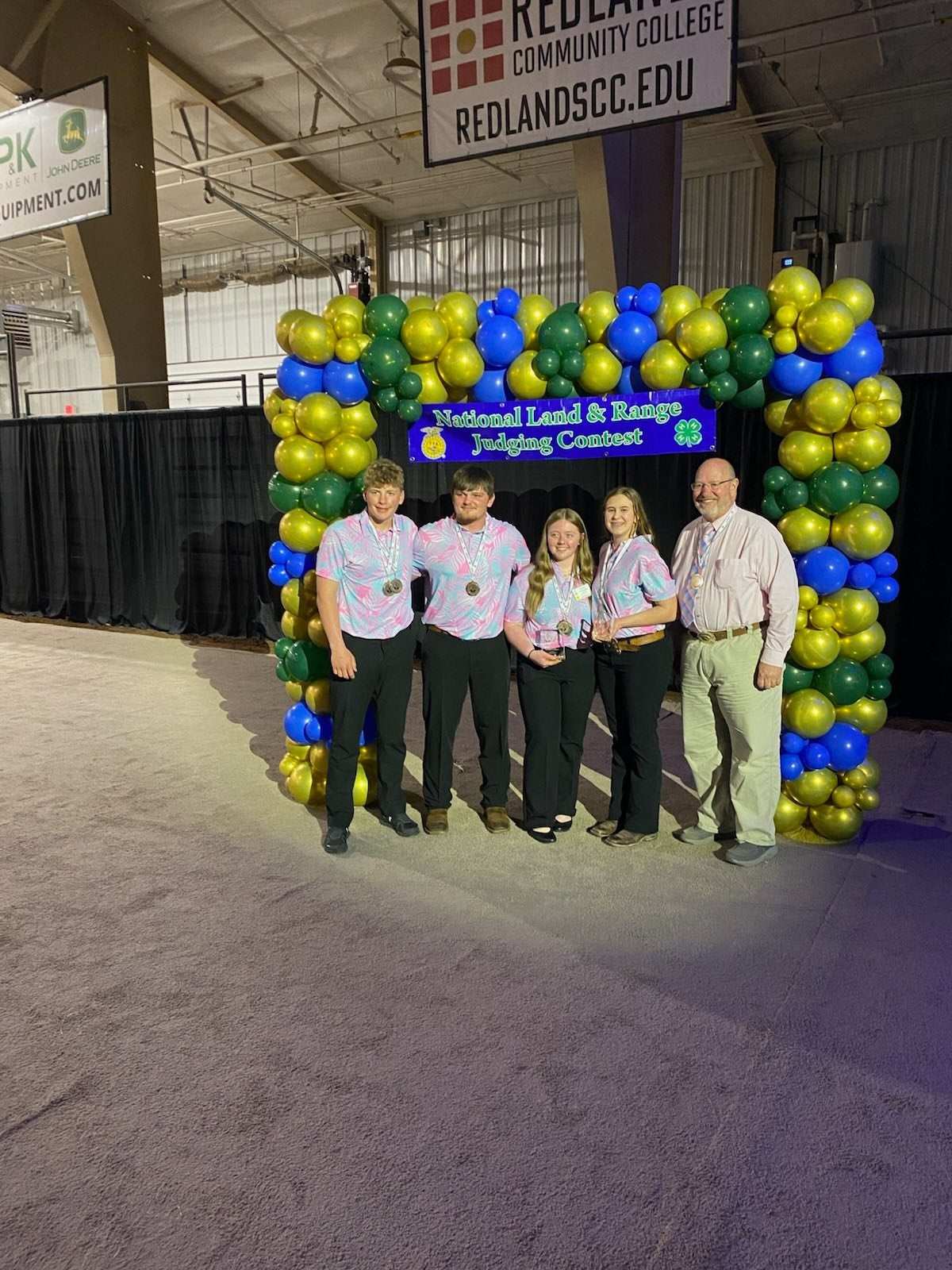 Four youth and an adult coach stand under a blue and green balloon arch
