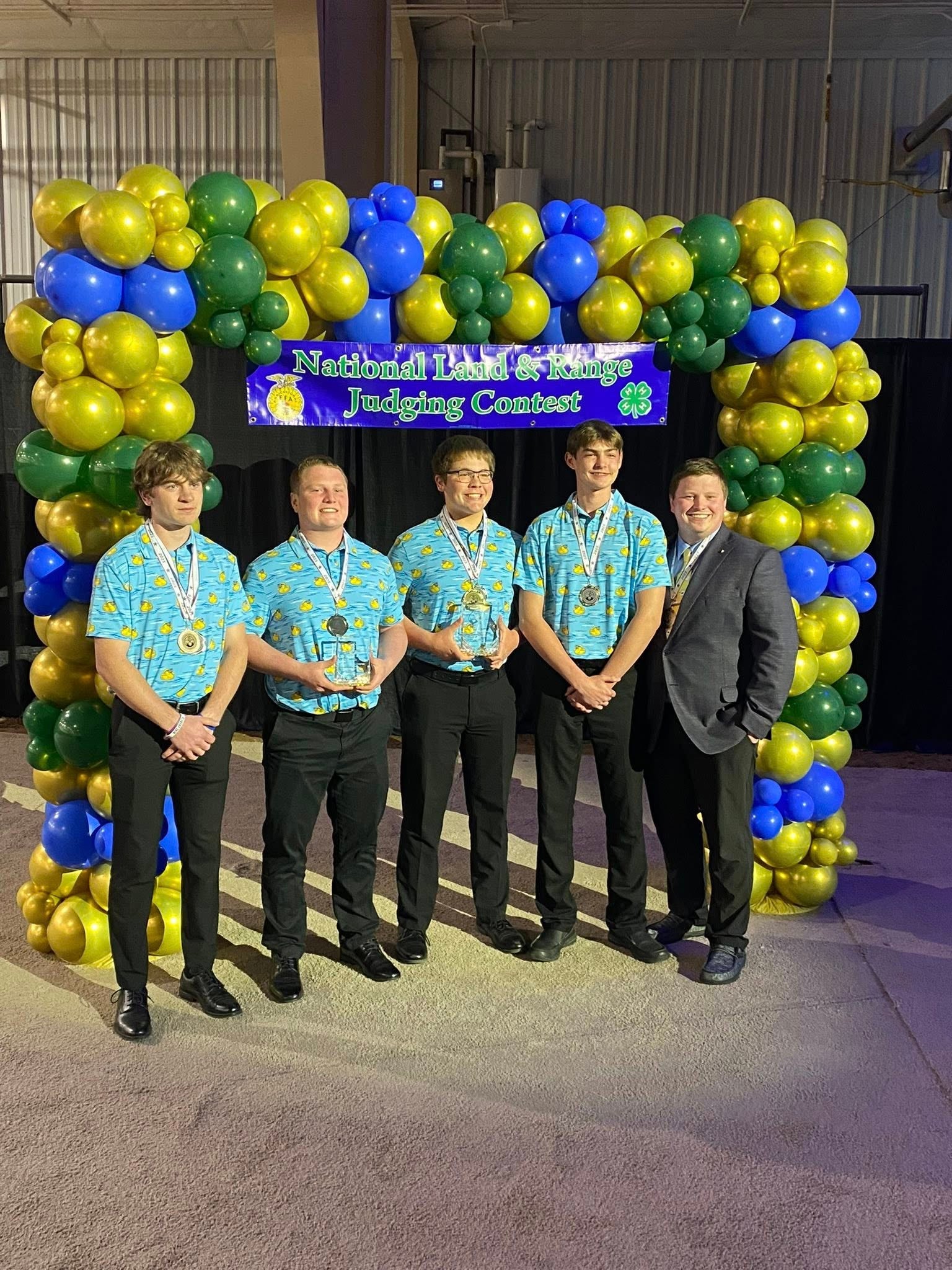Four teenage boys and a man stand under a blue and green balloon arch with a banner that reads &quot;National Land and Range Judging Contest&quot;