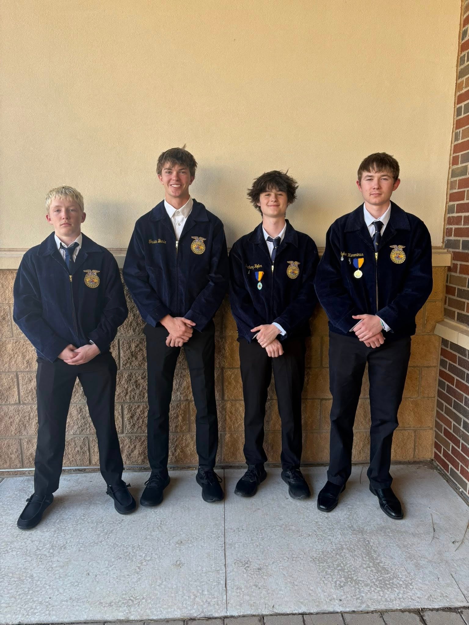 Four teenage boys in matching blue FFA jackets pose in front of a wall