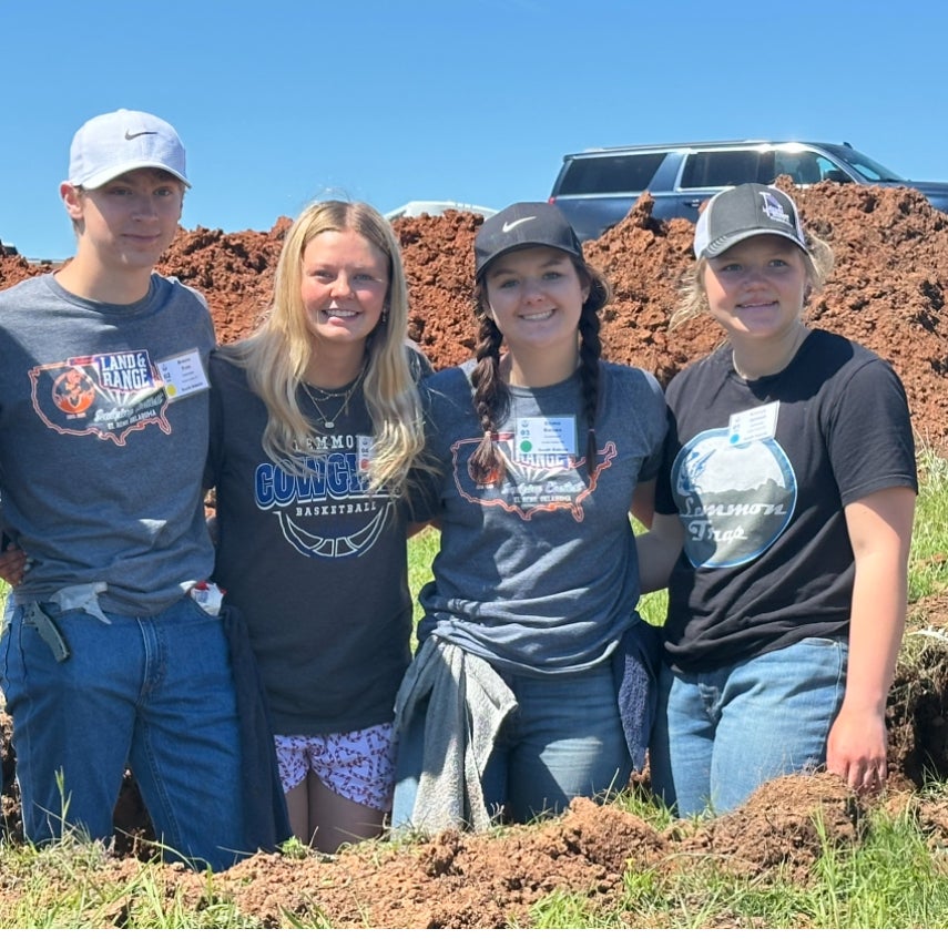 Four teenagers stand in front of a pile of dirt
