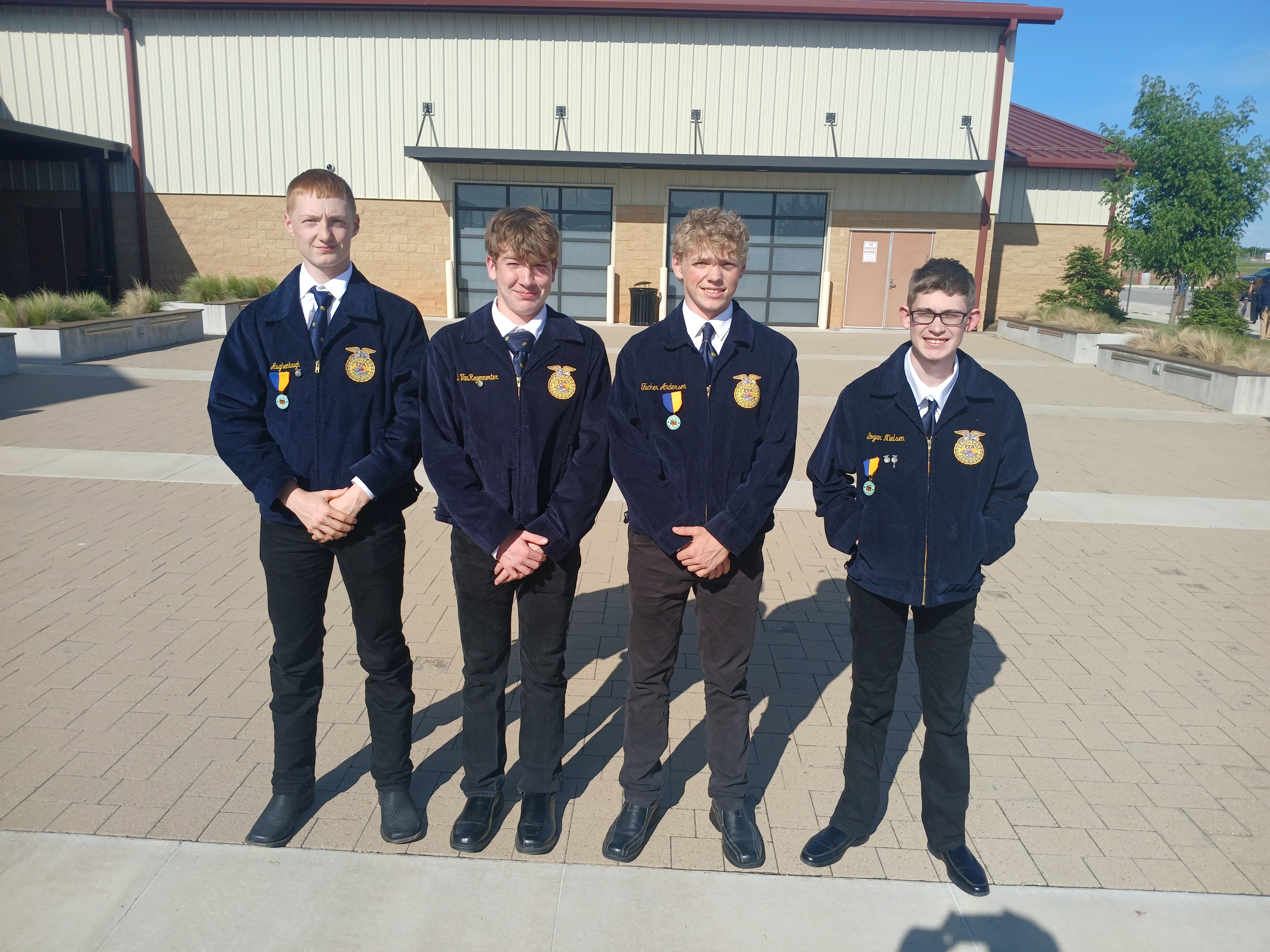 Four teenage boys in matching blue FFA jackets pose outside