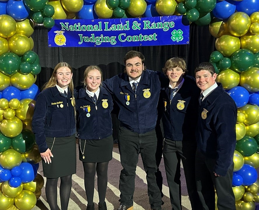 Five youth in FFA jackets stand under a blue and green balloon arch