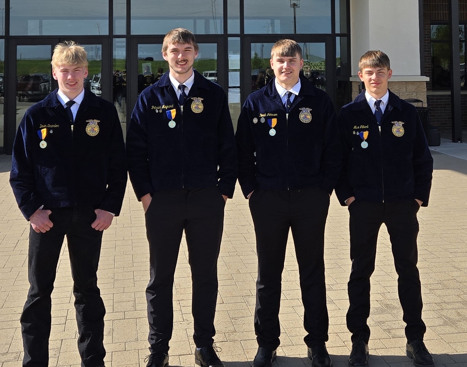 Four teenage boys in FFA jackets stand outside a building