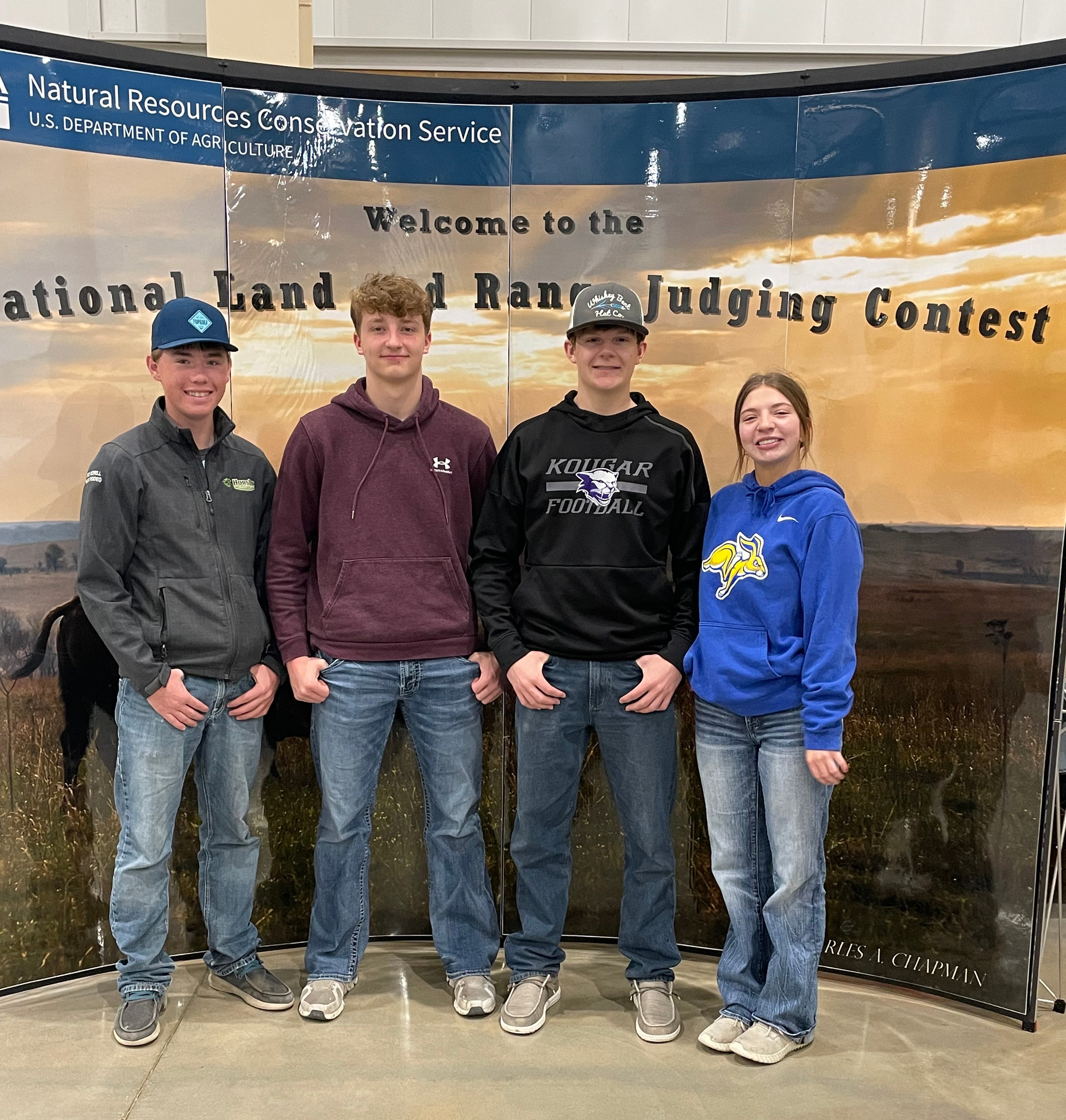 Four youth in hoodies stand in front of a display that says &quot;Welcome to the National Land and Range Judging Contest&quot;