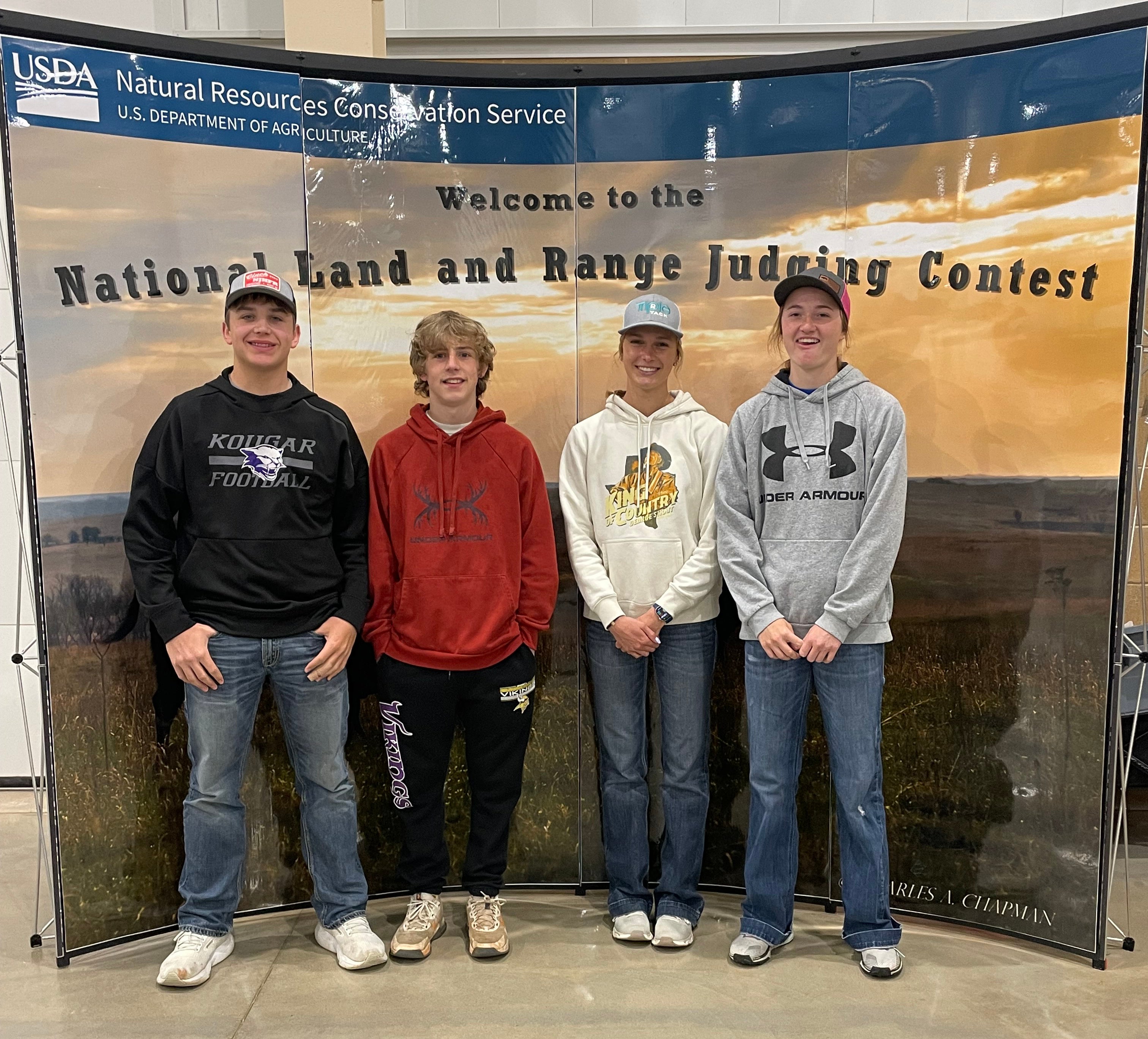 Four youth stand in front of a display that says "Welcome to the National Land and Range Judging Contest"