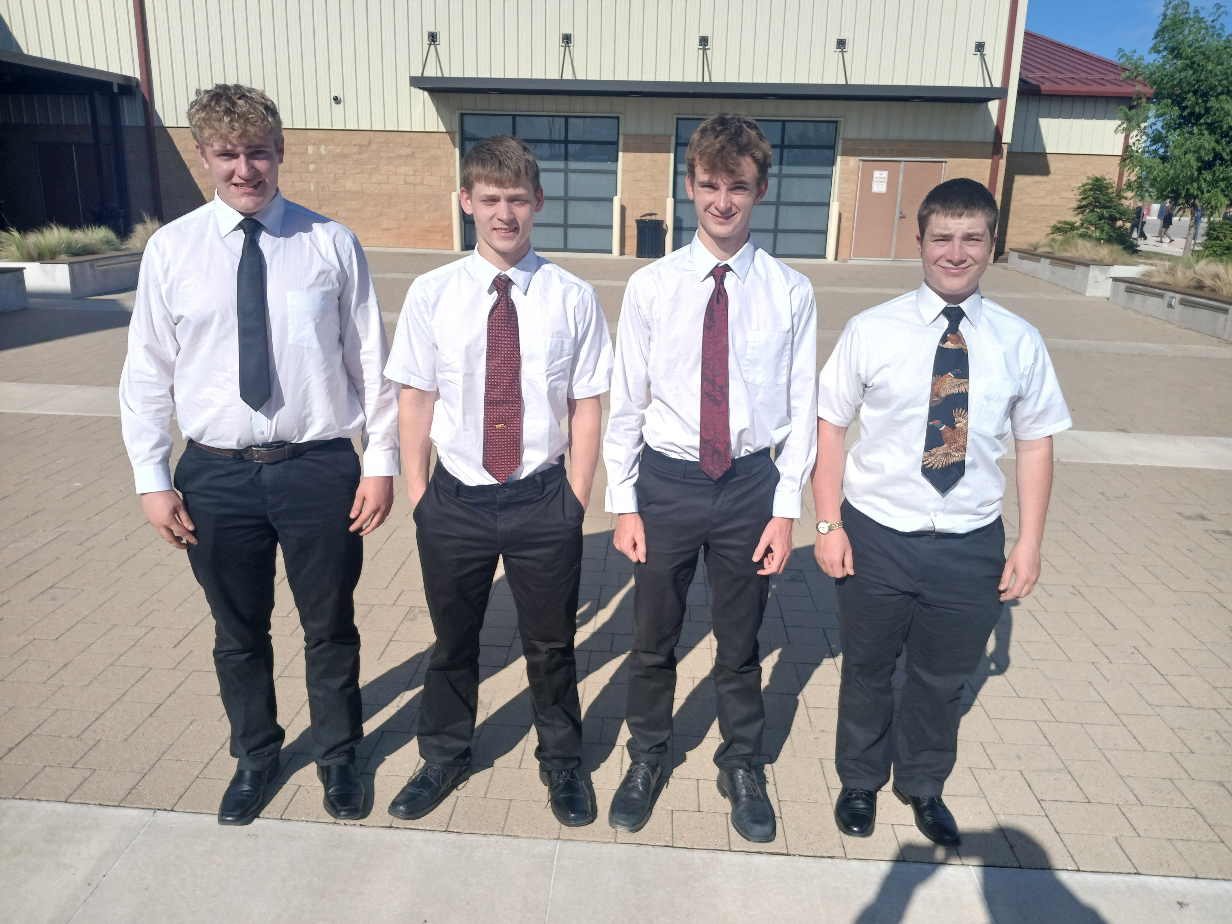 Four men in white button-down shirts, ties and black slacks stand outside for a team photo