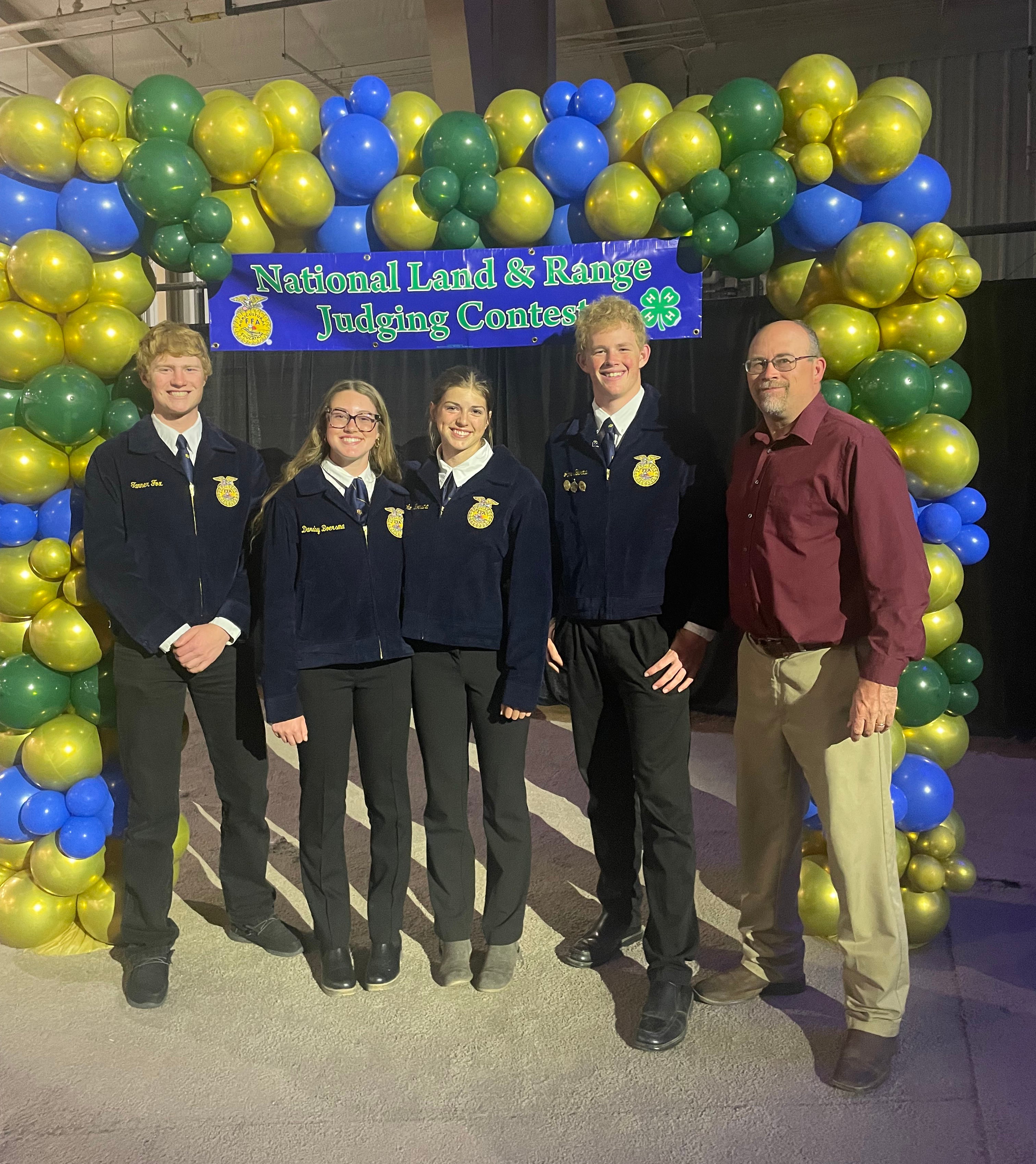 Four youth in blue FFA jackets and their coach pose for a team photo under a blue and green balloon arch