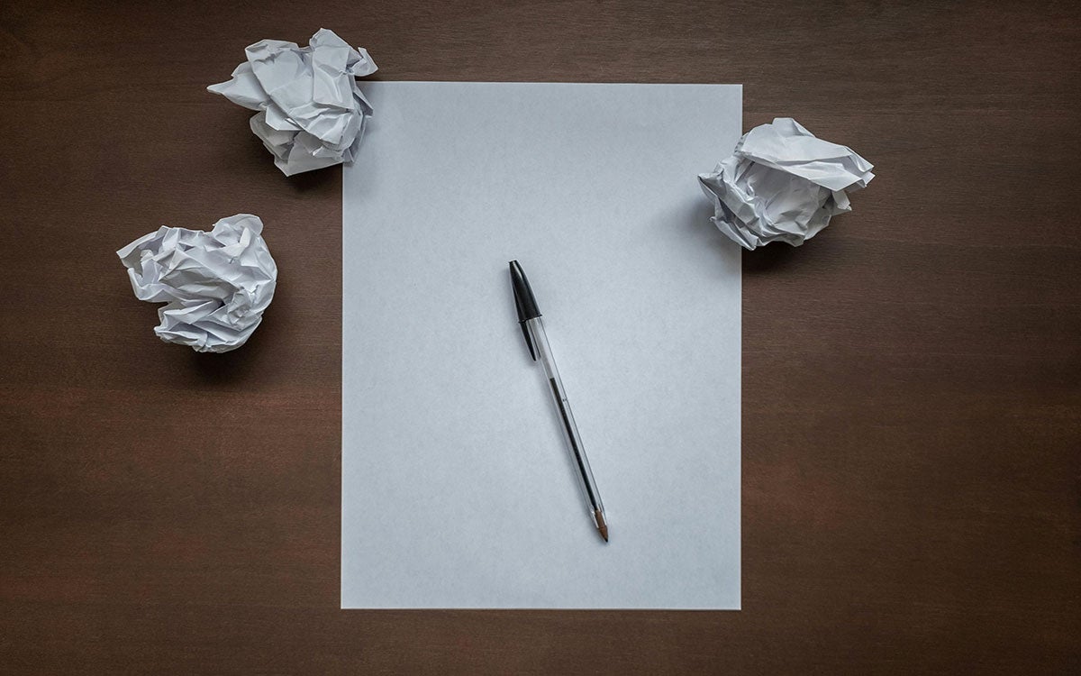 Crumpled up pieces of paper and a notepad on a desk.