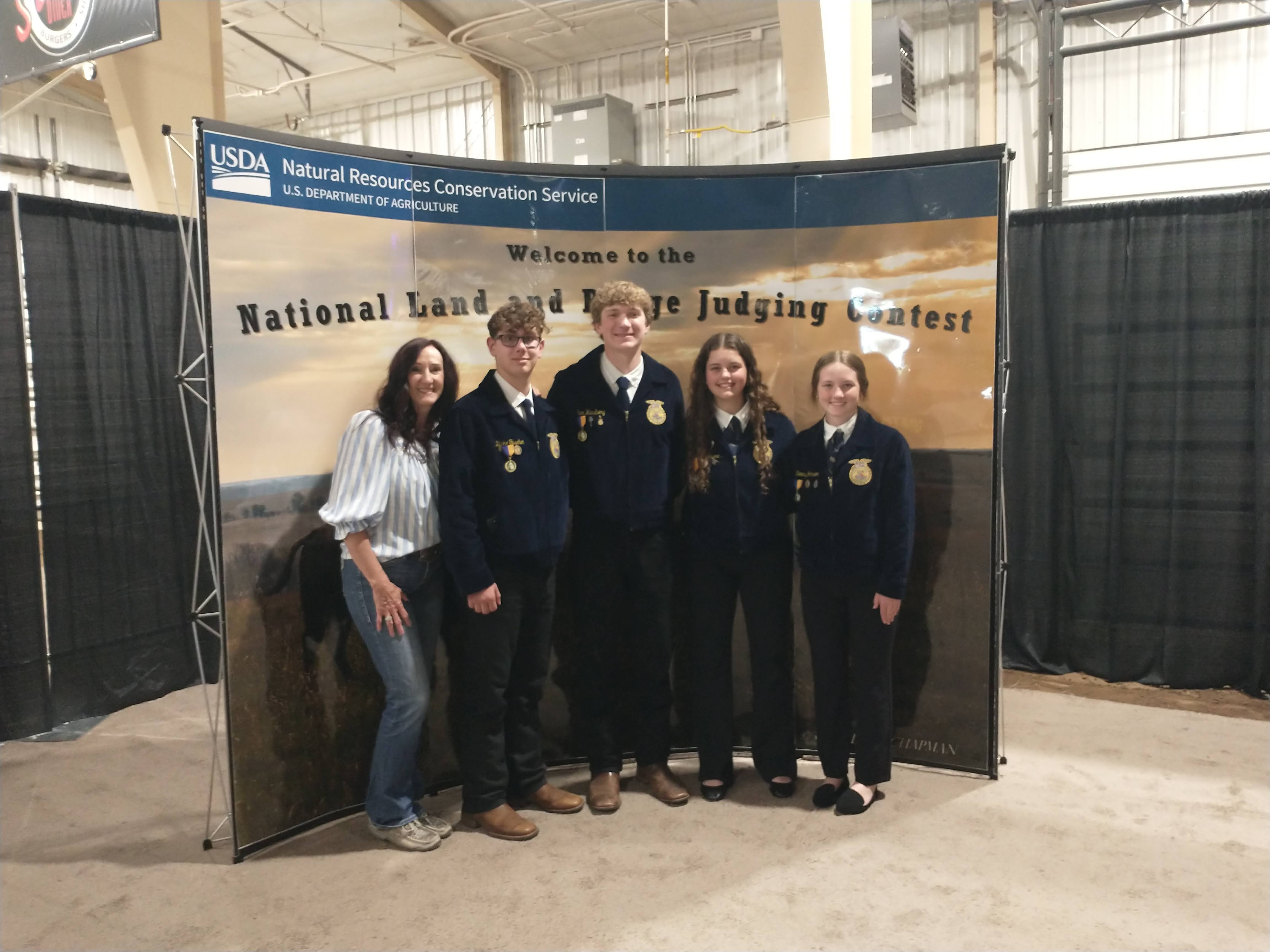 four youth in matching FFA jackets pose with their coach for a team photo