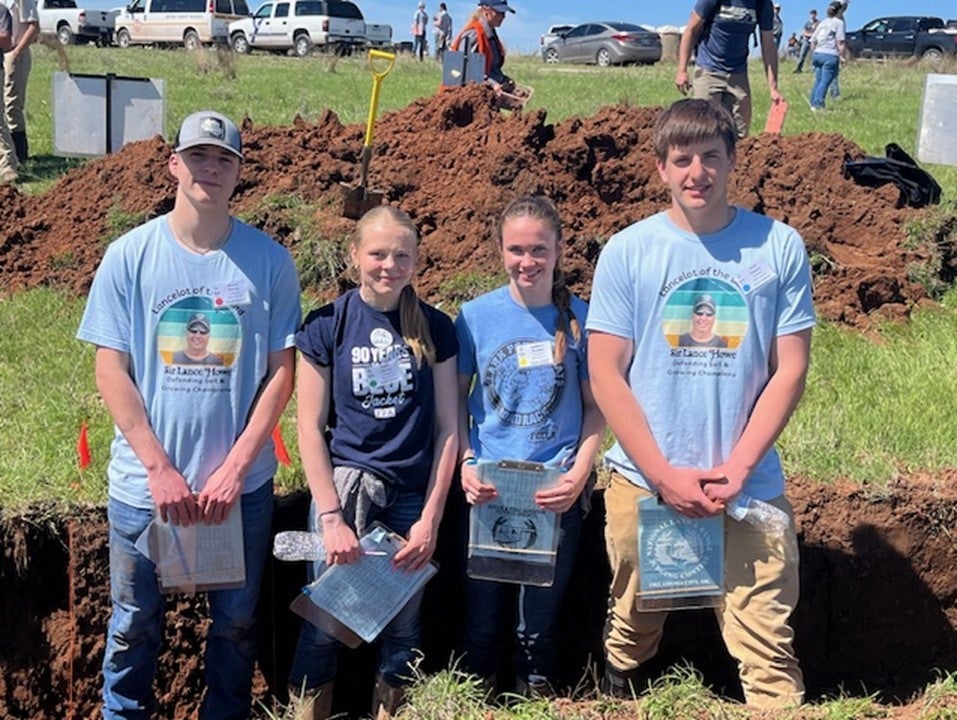Four youth stand inside a shallow hole with clipboards used to evaluate a homesite