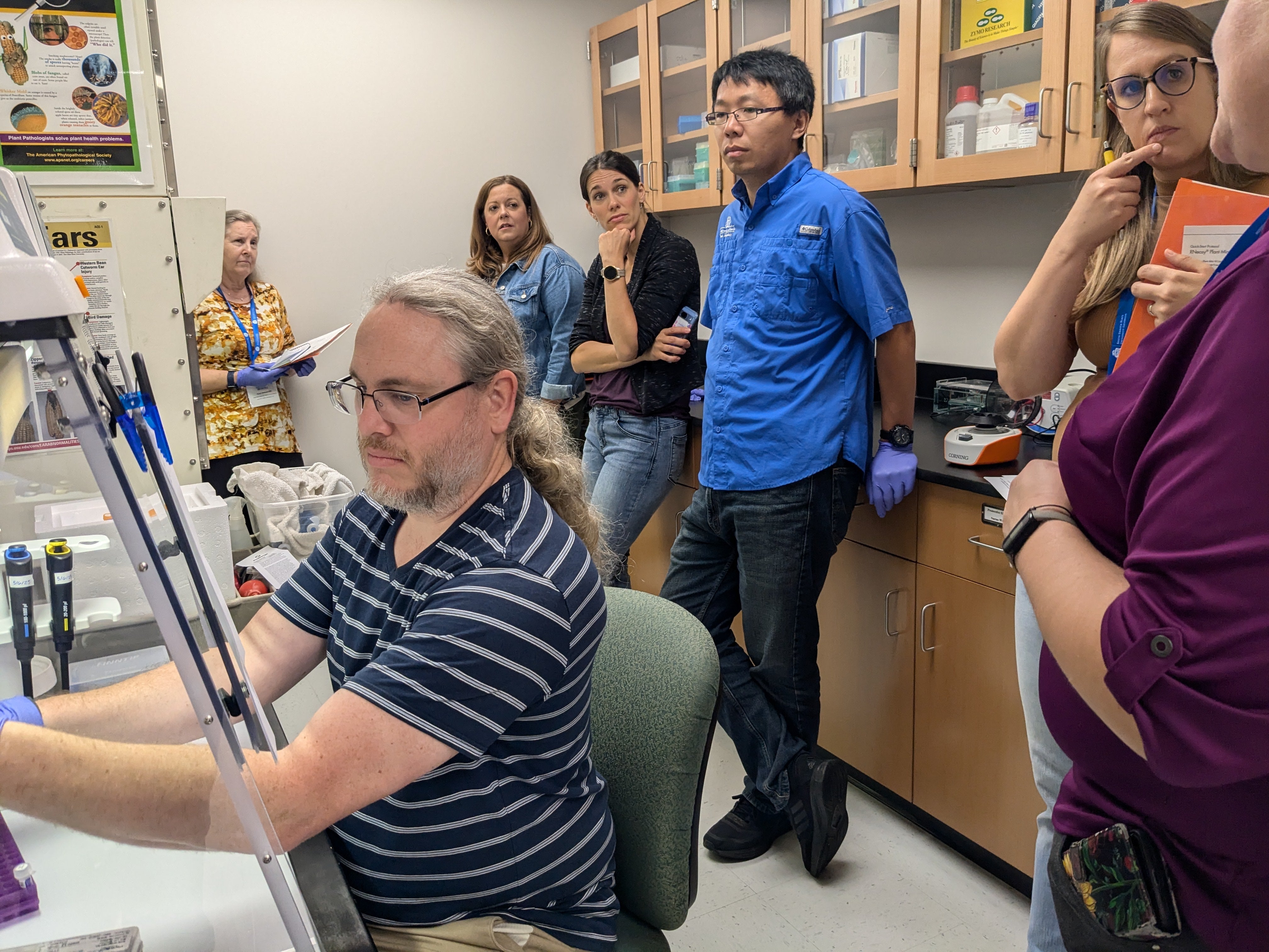 People stand in a classroom watching a man work with lab equipment