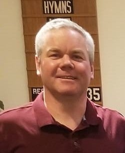 A man in a red collared shirt smiles for the camera