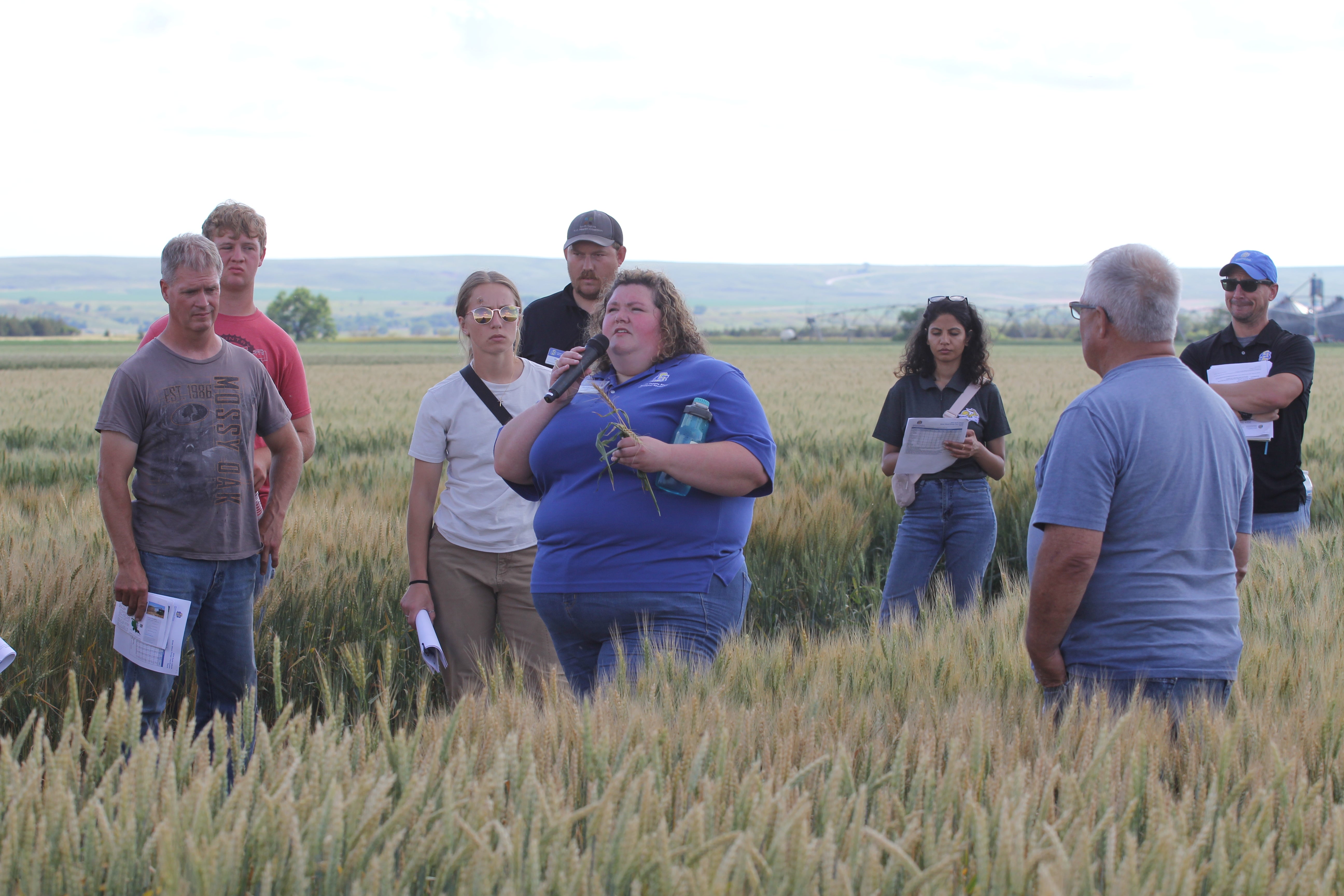 People stand in a field listening to a person speak