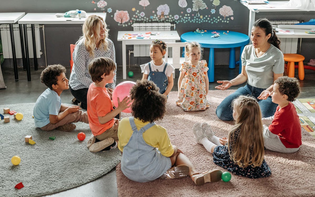 Teachers at a daycare instructing a group of children at various ages and stages.