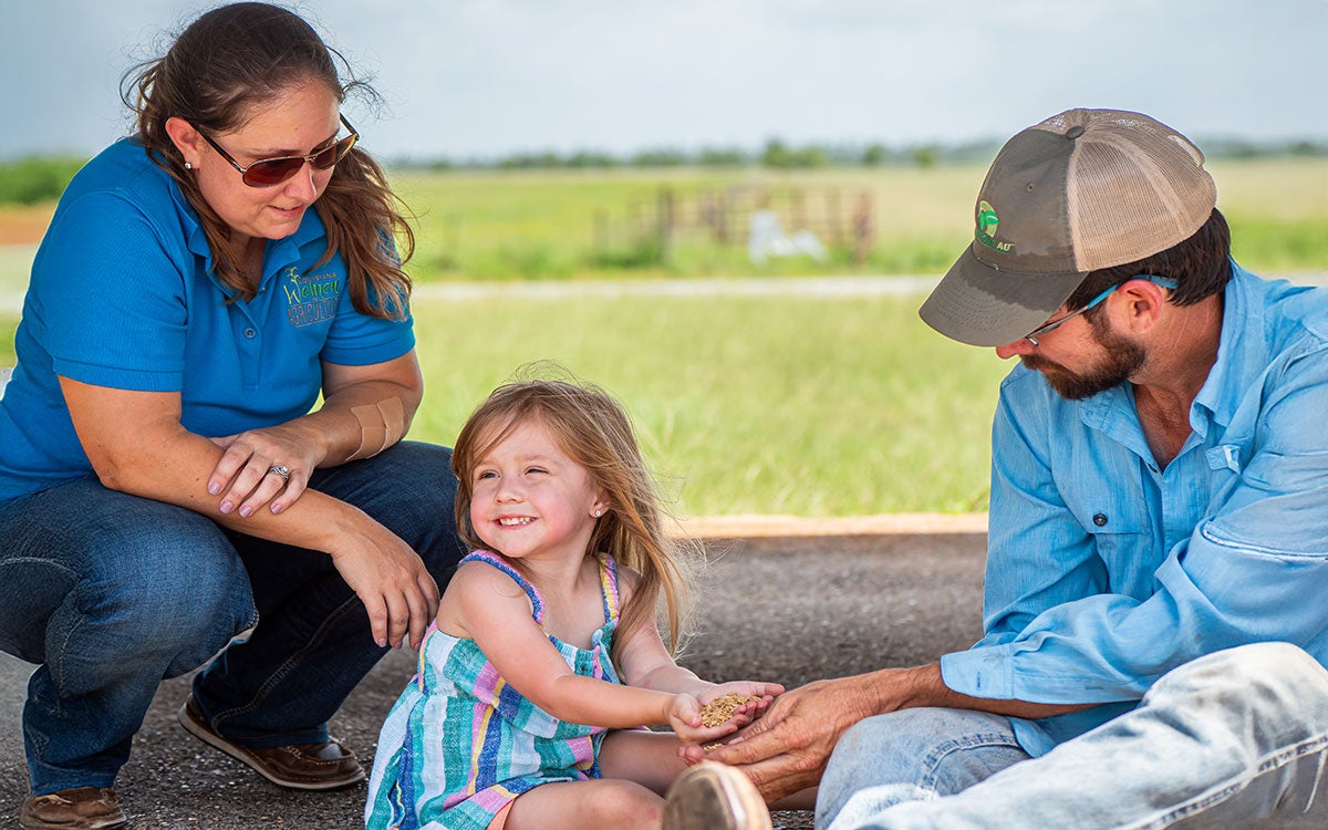 Mother, father, and young daughter gathered in a farmyard.