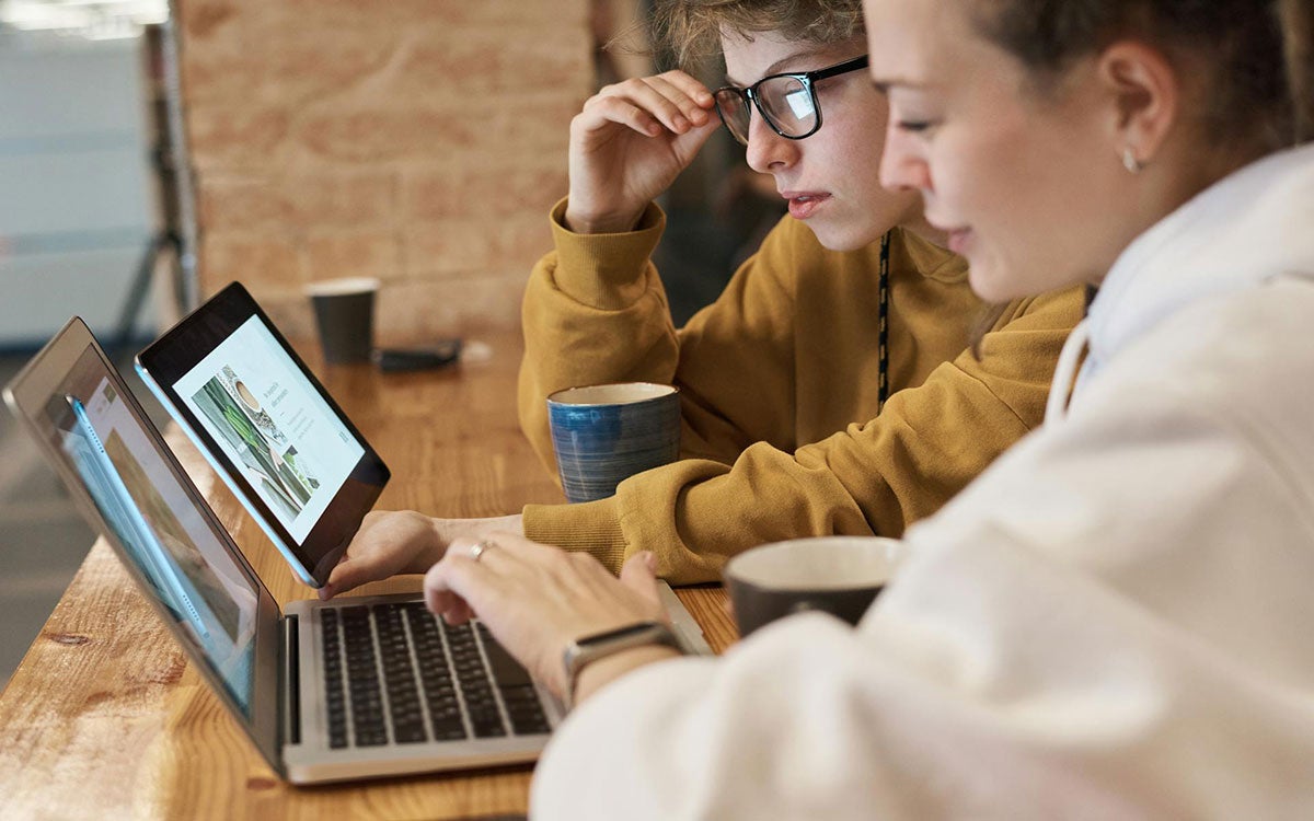 Two young adults viewing information on a tablet and computer.