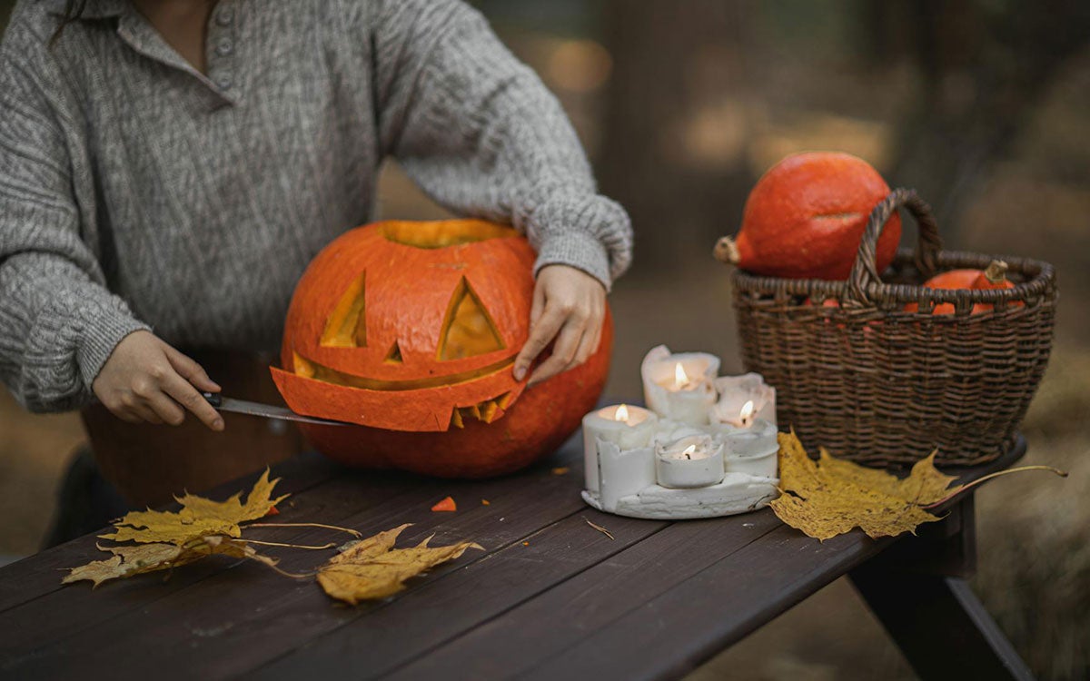 Person carving a pumpkin on an outdoor picnic bench.