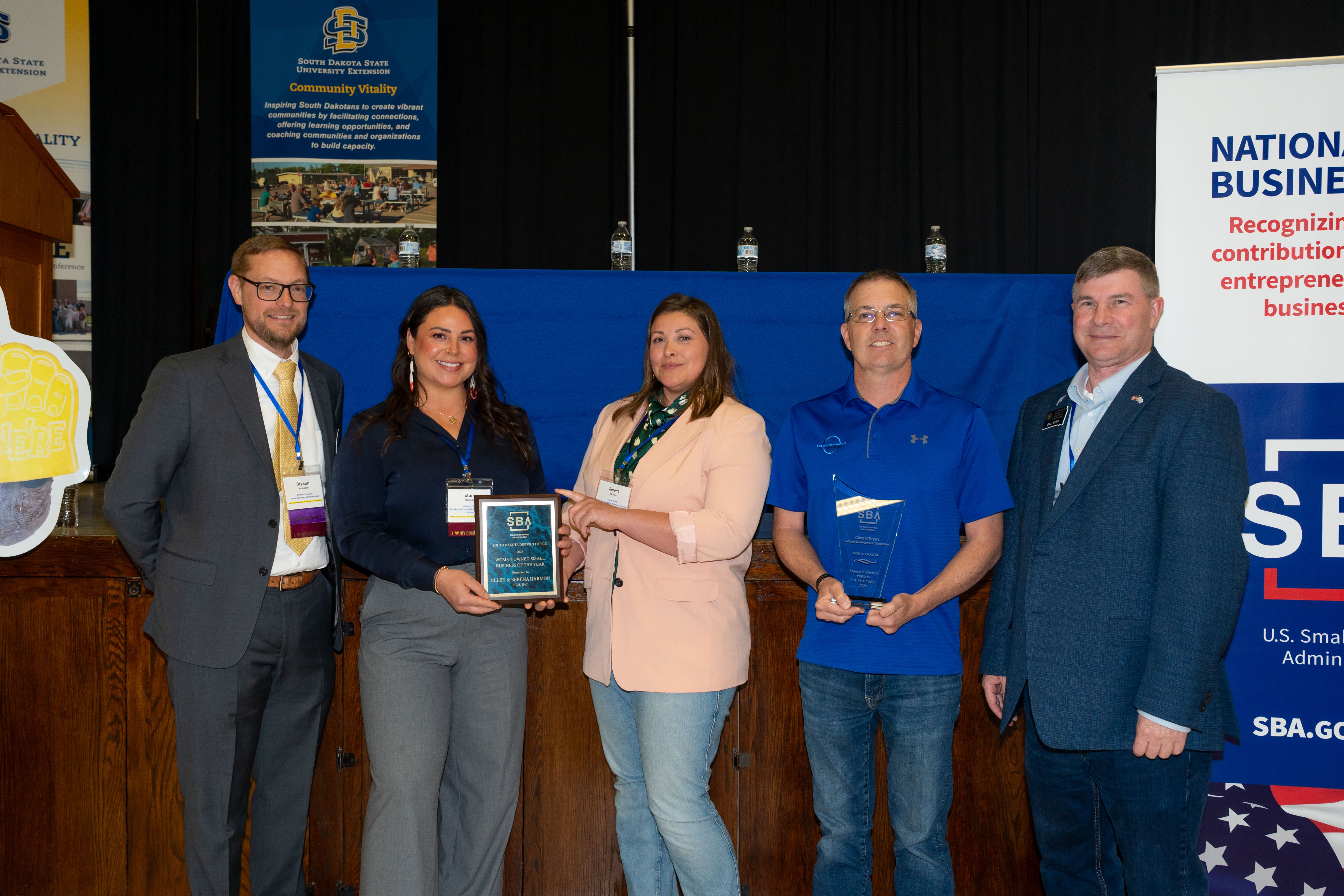 Five people smile for the camera, three of them holding award plaques