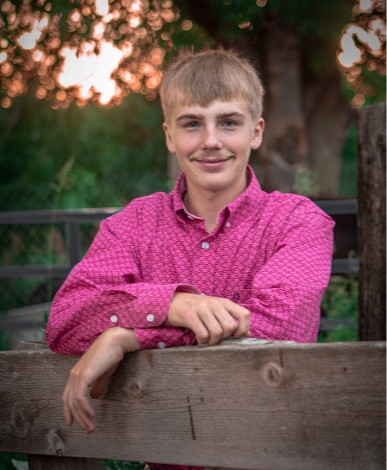 A young man in a pink long-sleeved shirt smiles for a portrait