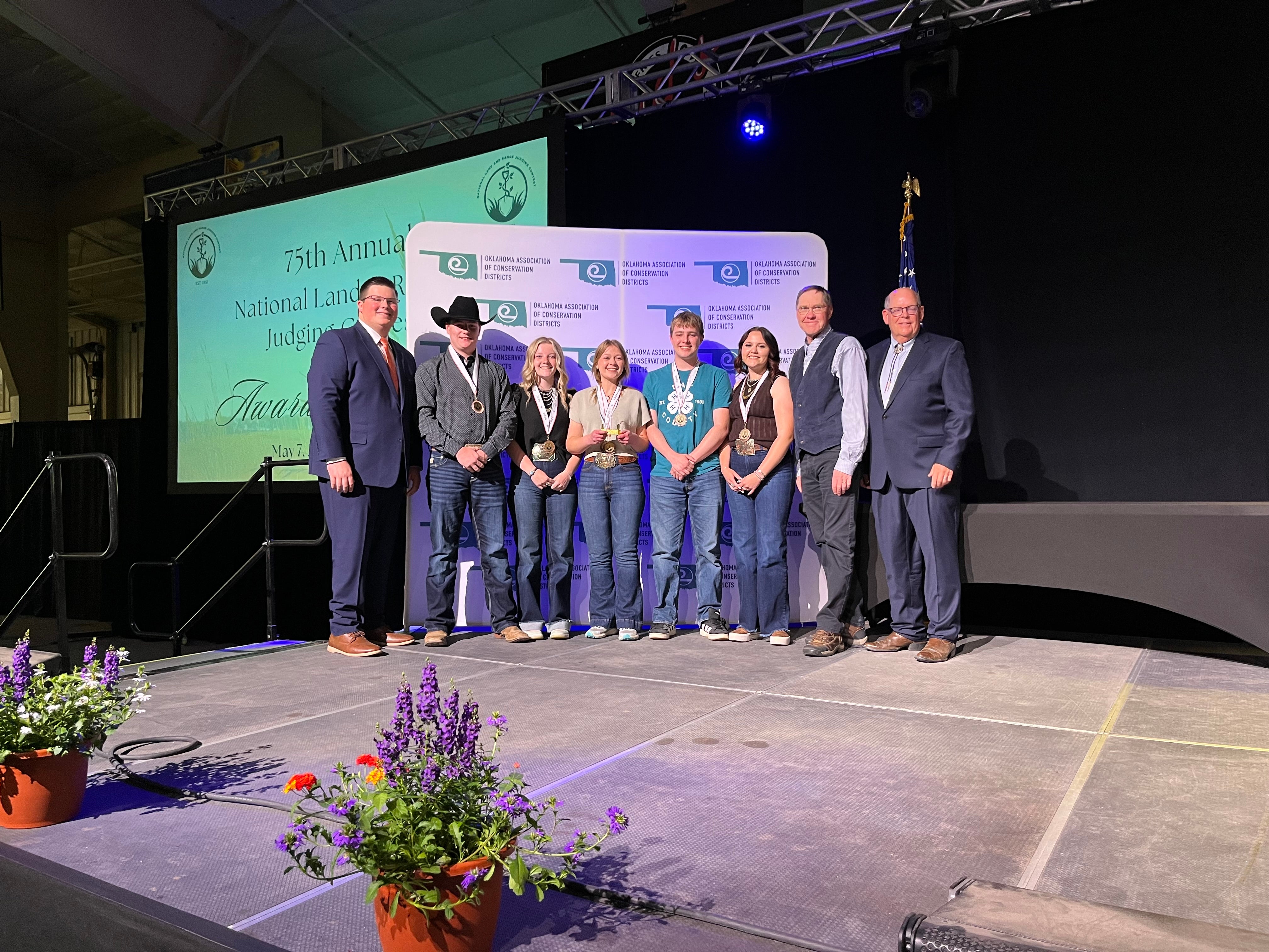 Eight people smile on a stage wearing fourth-place medals