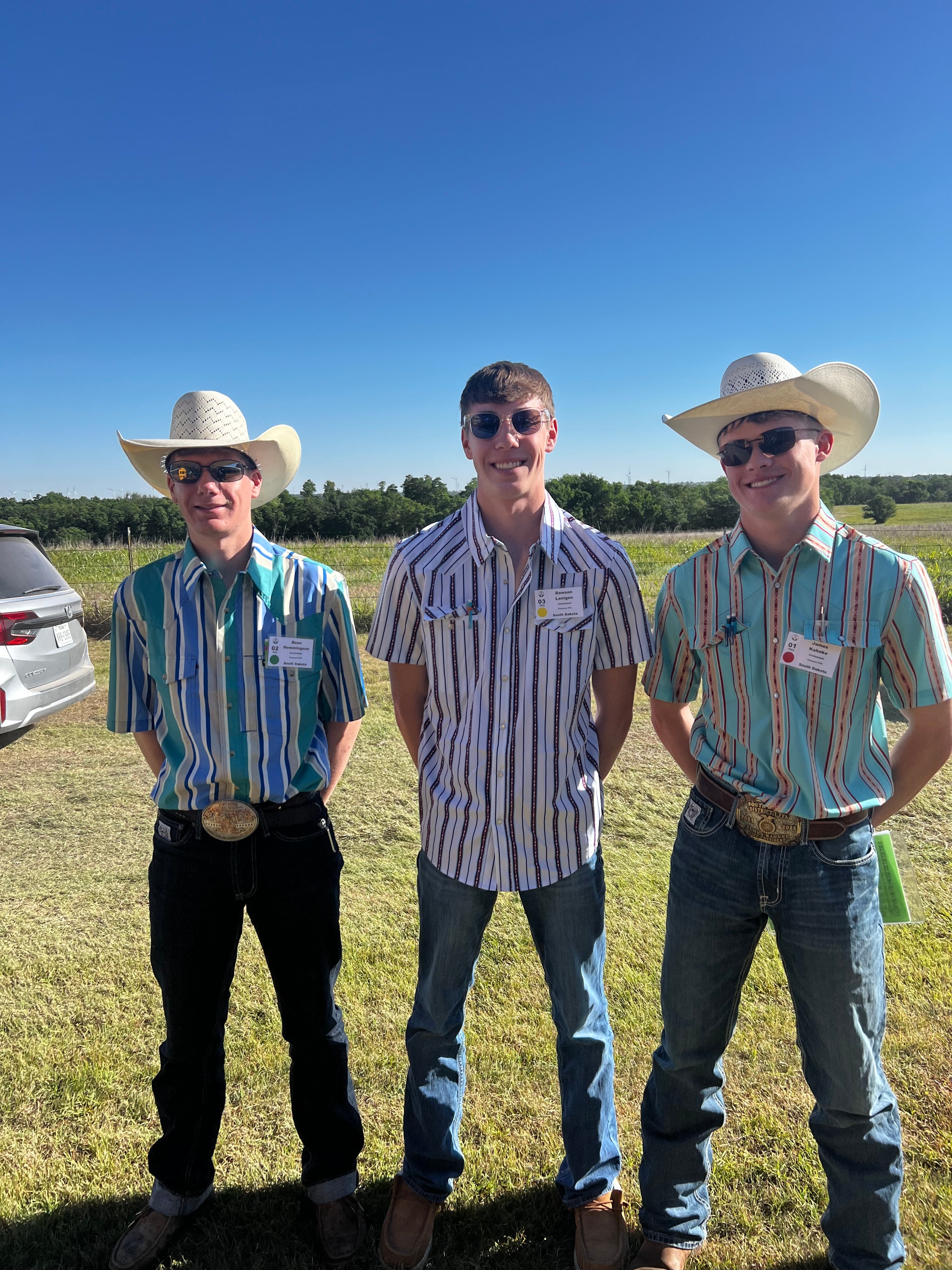 Three boys in striped shirts smile standing outside in a pasture