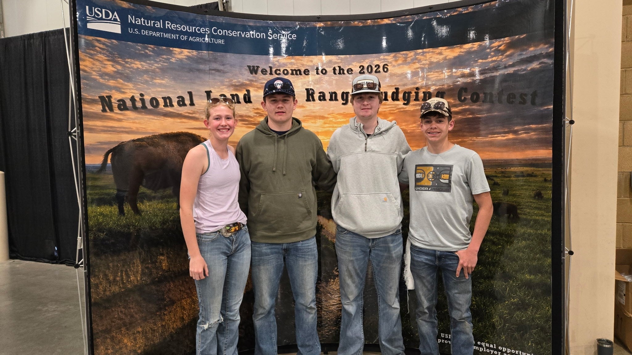 Four youth stand in front of a National Land and Range Judging Contest photo backdrop