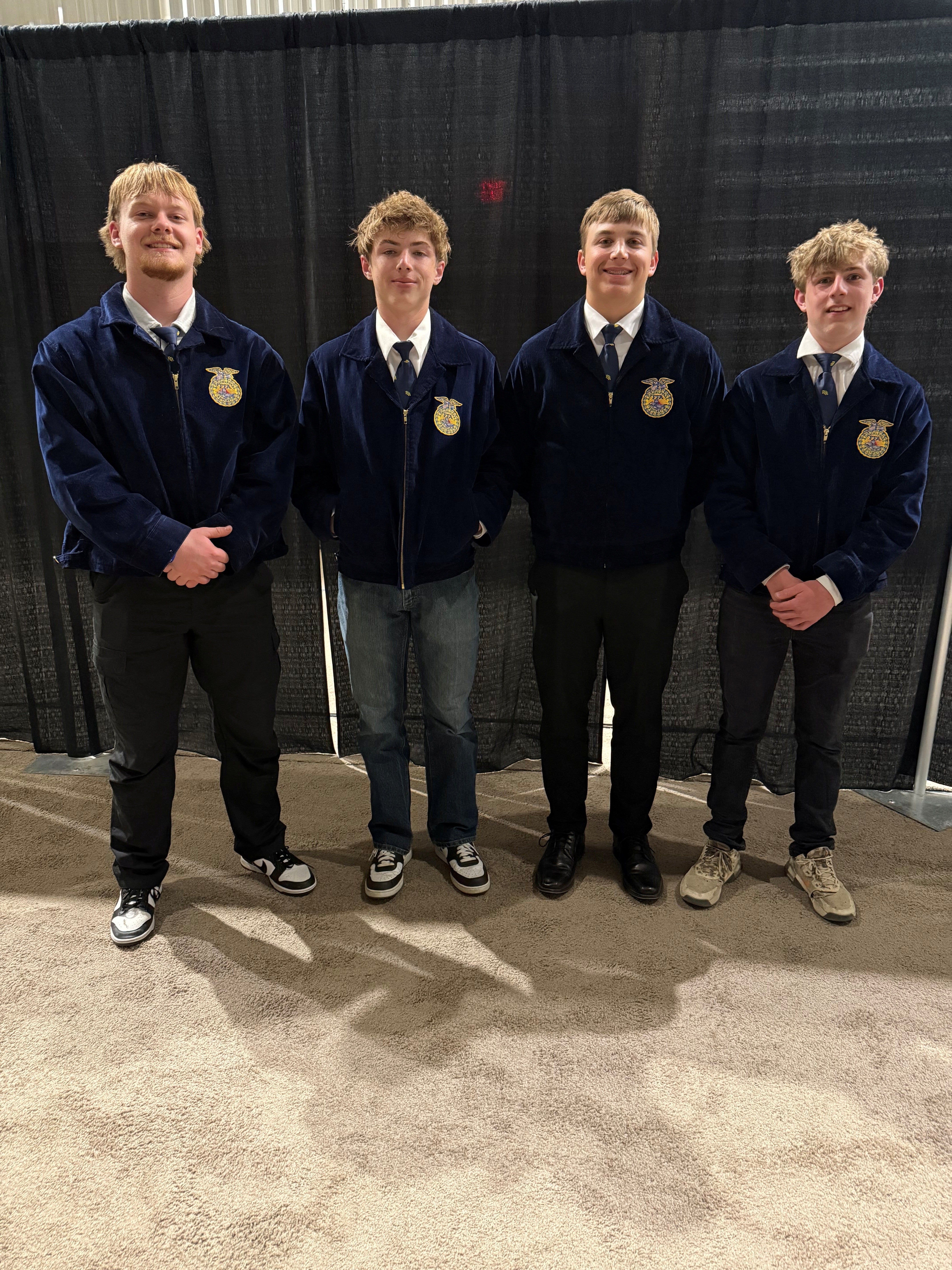 Four teenage boys wearing matching FFA jackets smile for the camera