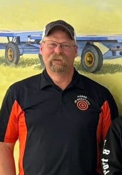 A man with a mustache wearing a baseball cap smiles for a photo