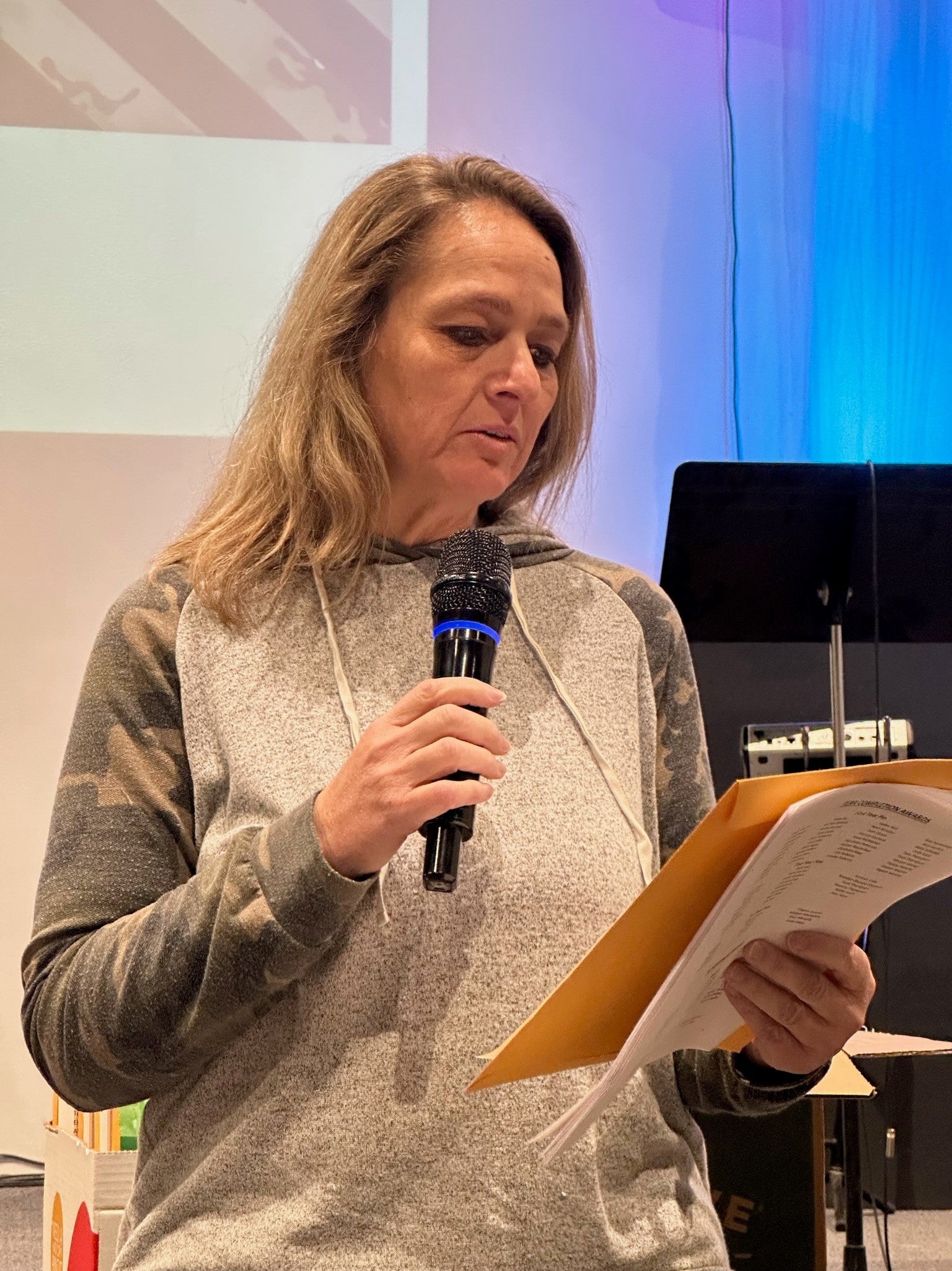 A woman holds a microphone and reads from a piece of paper